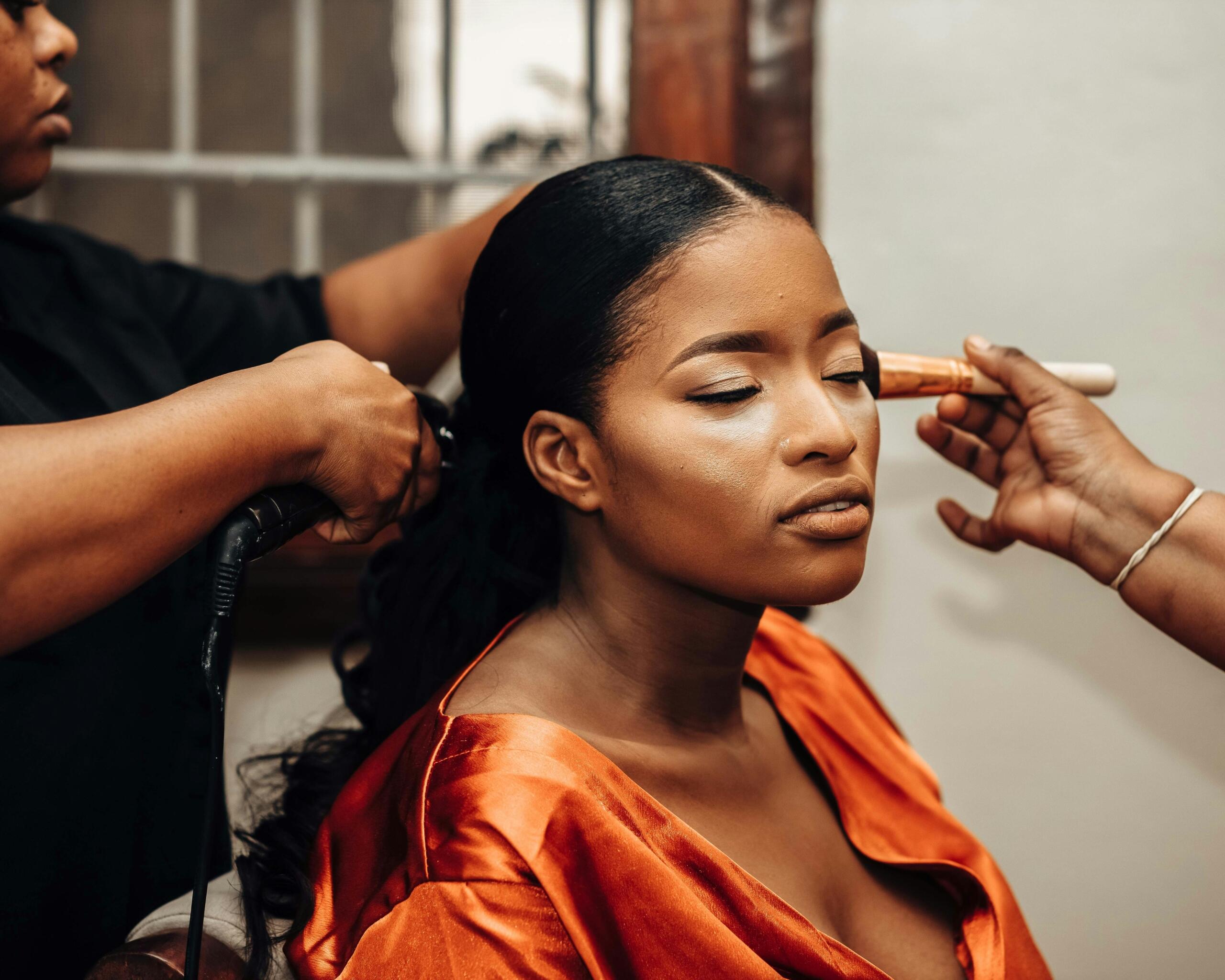 woman sitting in a chair while a makeup artist does her hair and a hair stylist does her hair