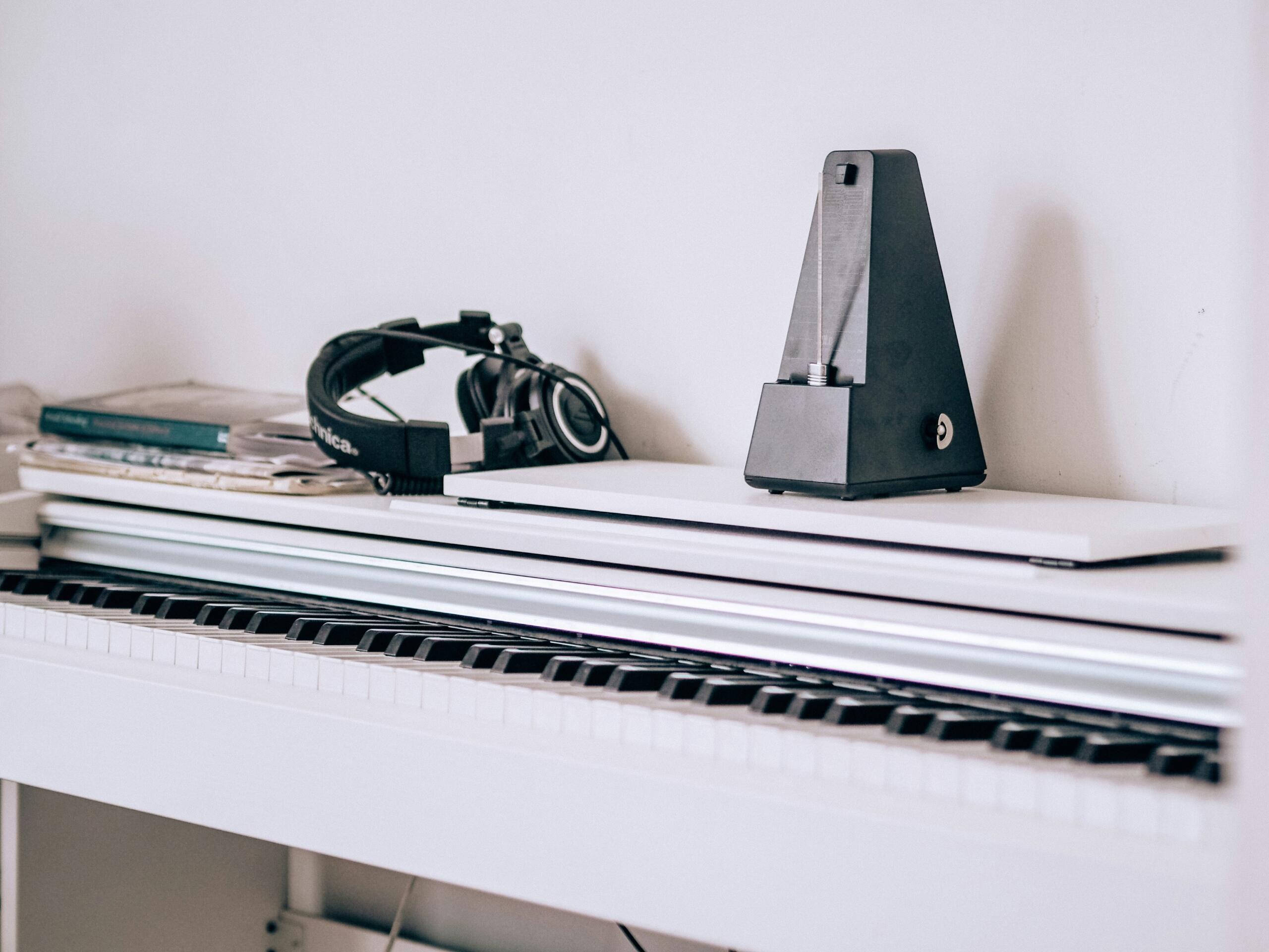 metronome and headphones placed on top of a white piano