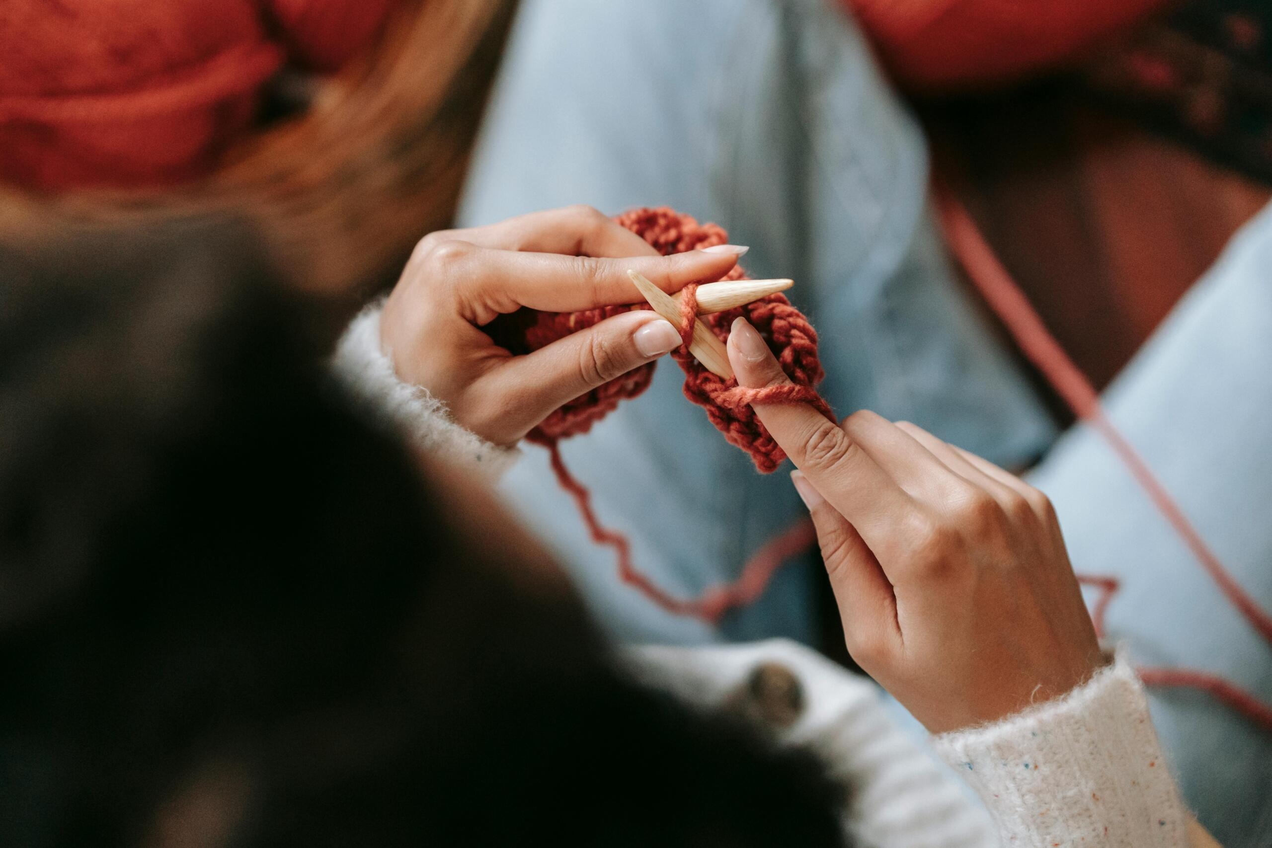 woman sitting and knitting using wooden knitting needles