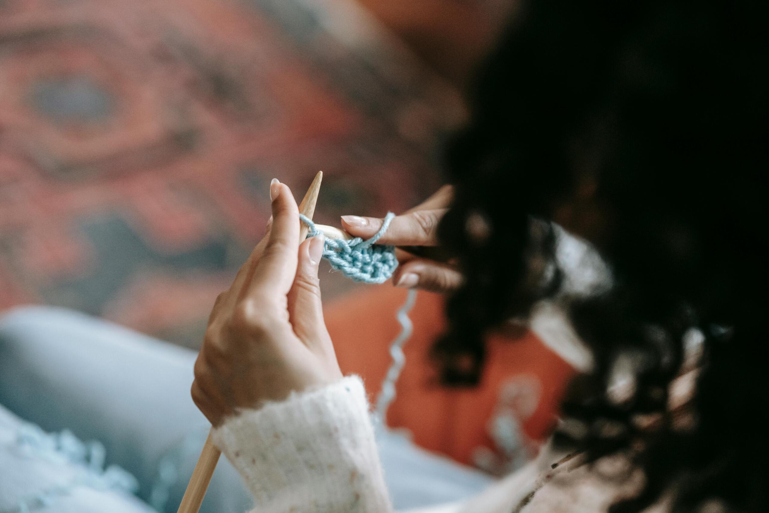 woman sitting and knitting using wooden knitting needles and blue yarn
