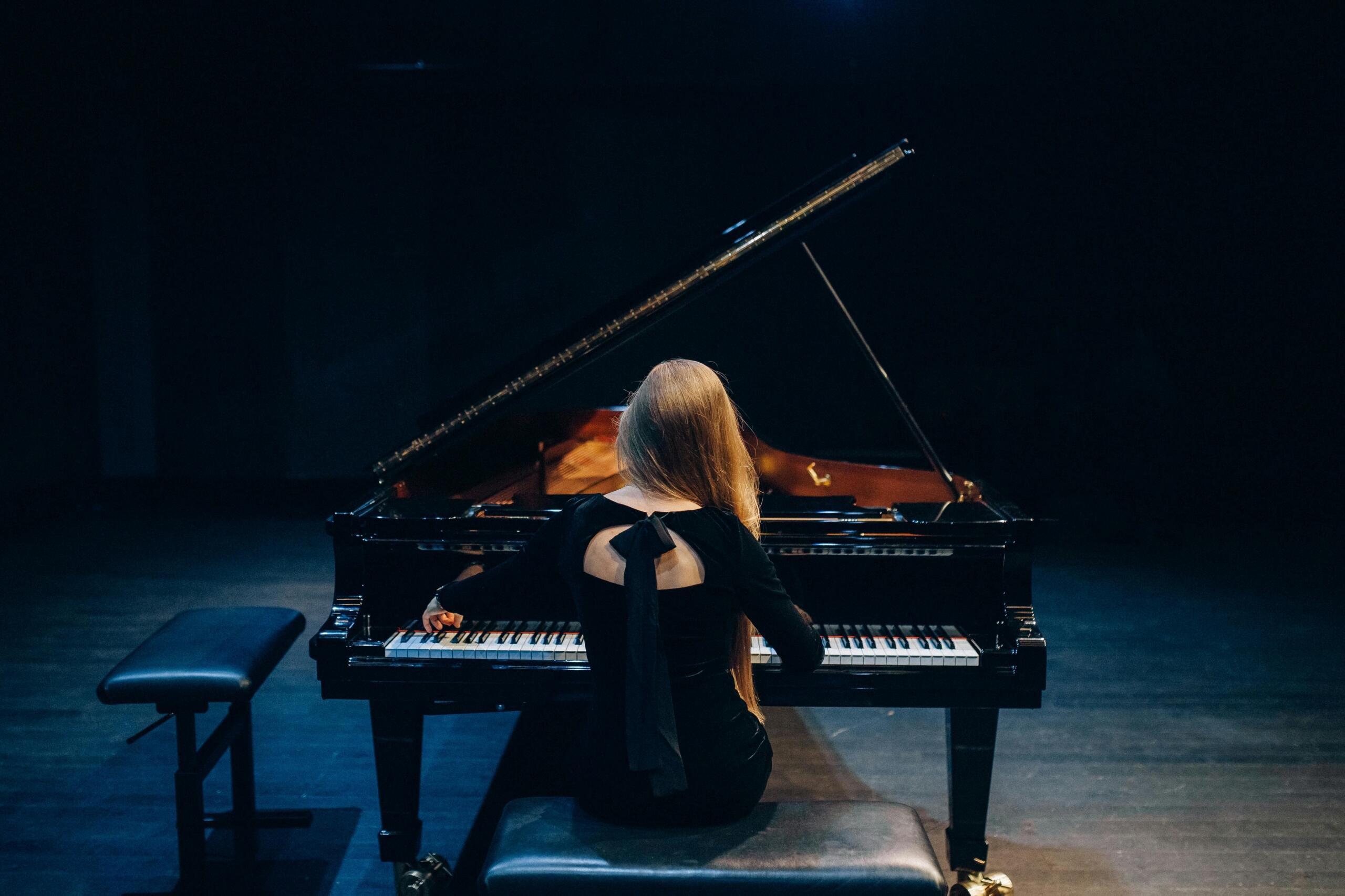 An elegant woman is seated at a grand piano for a recital. 