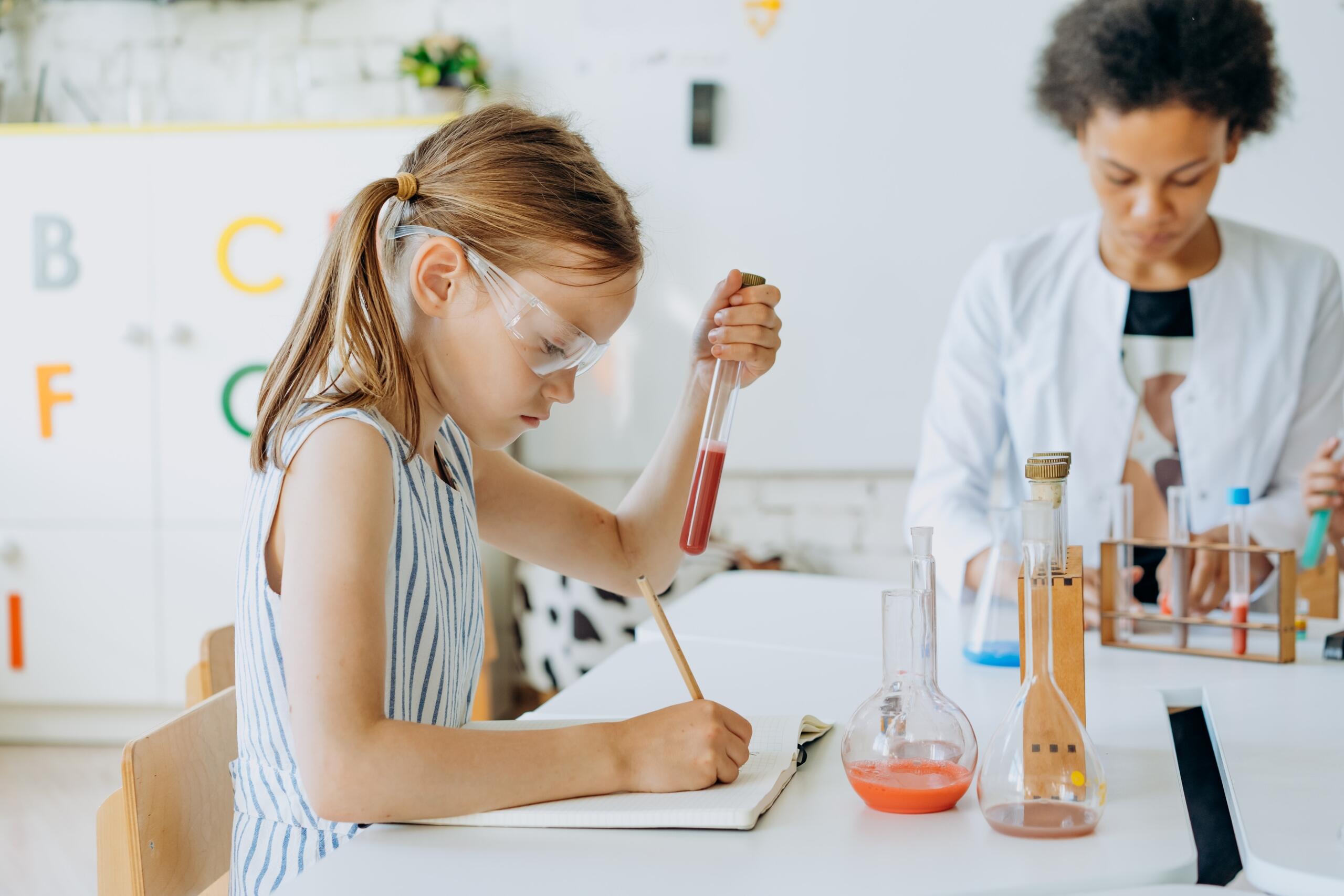 young girl working with chemistry equipment while private teacher supervises