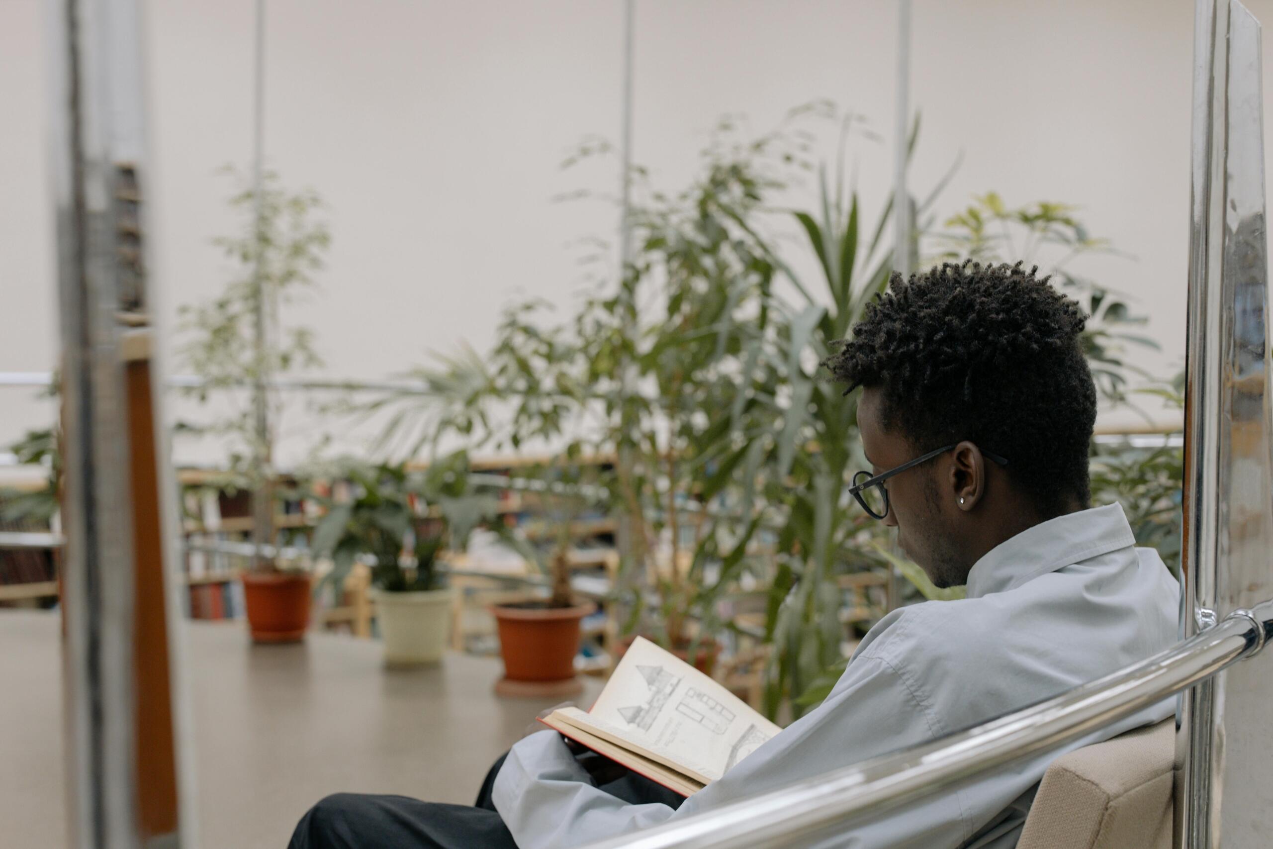 student reading a book, sitting in an empty space lined with plants