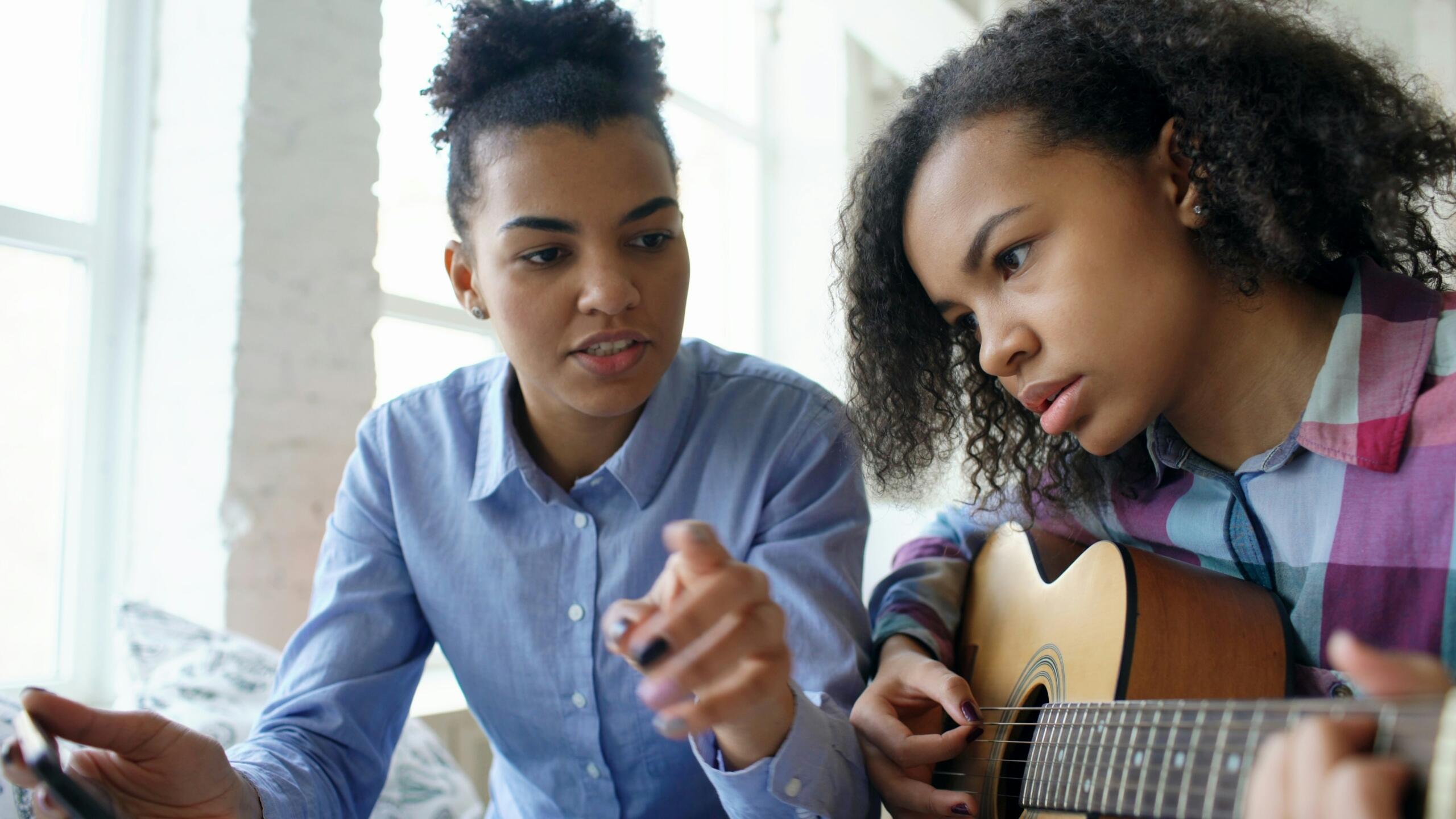 Tutor pointing a finger while student plays the guitar