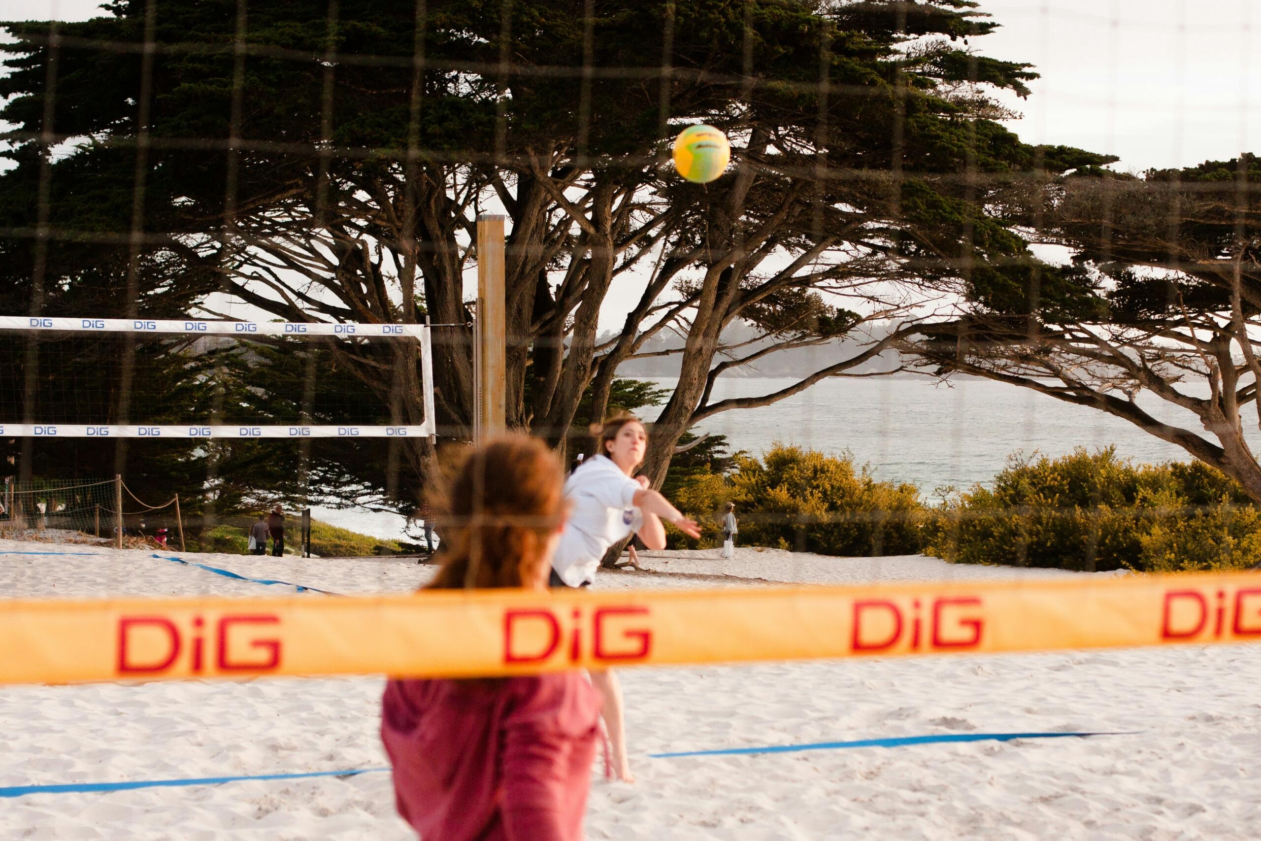 two girls playing volleyball on a white sand beach near trees
