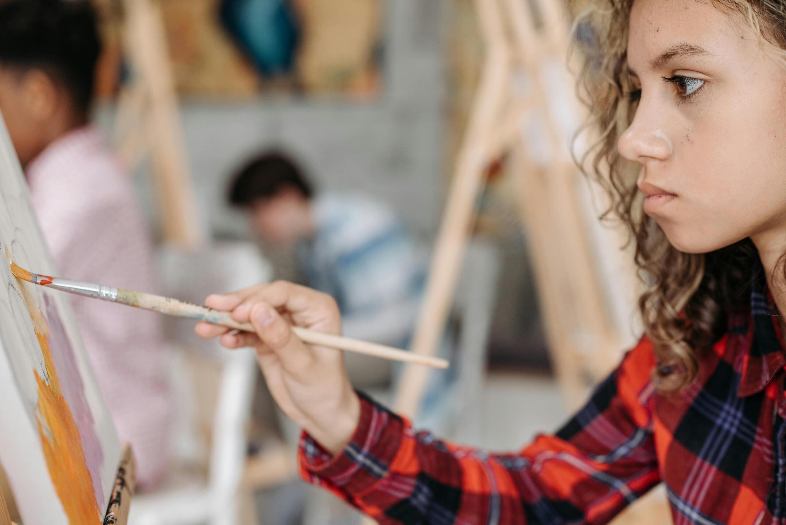girl in an art studio painting on a canvas with other students in the background