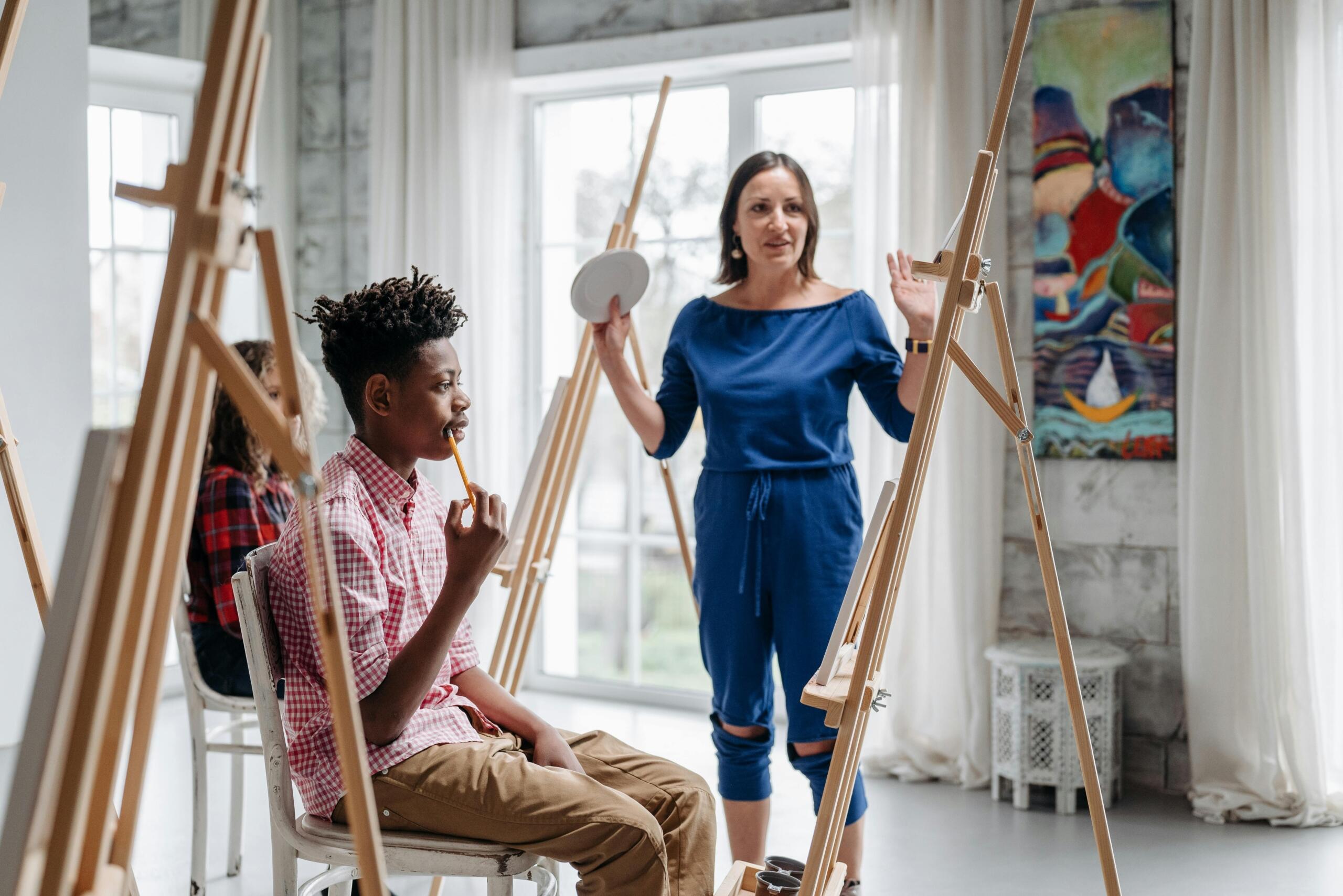 art teacher standing between students who are seated behind easels with canvasses