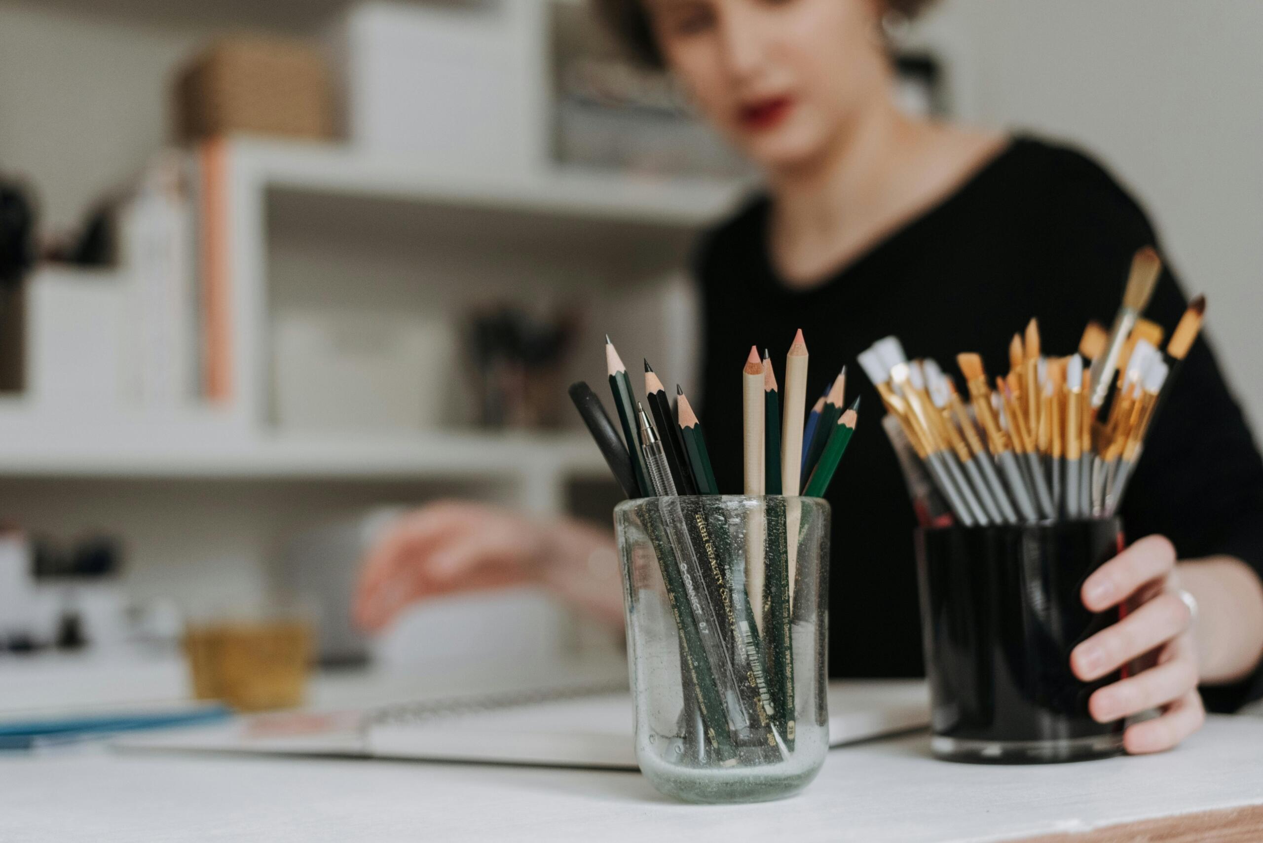 woman sketching reaching for a pot of paint brushes and pencils
