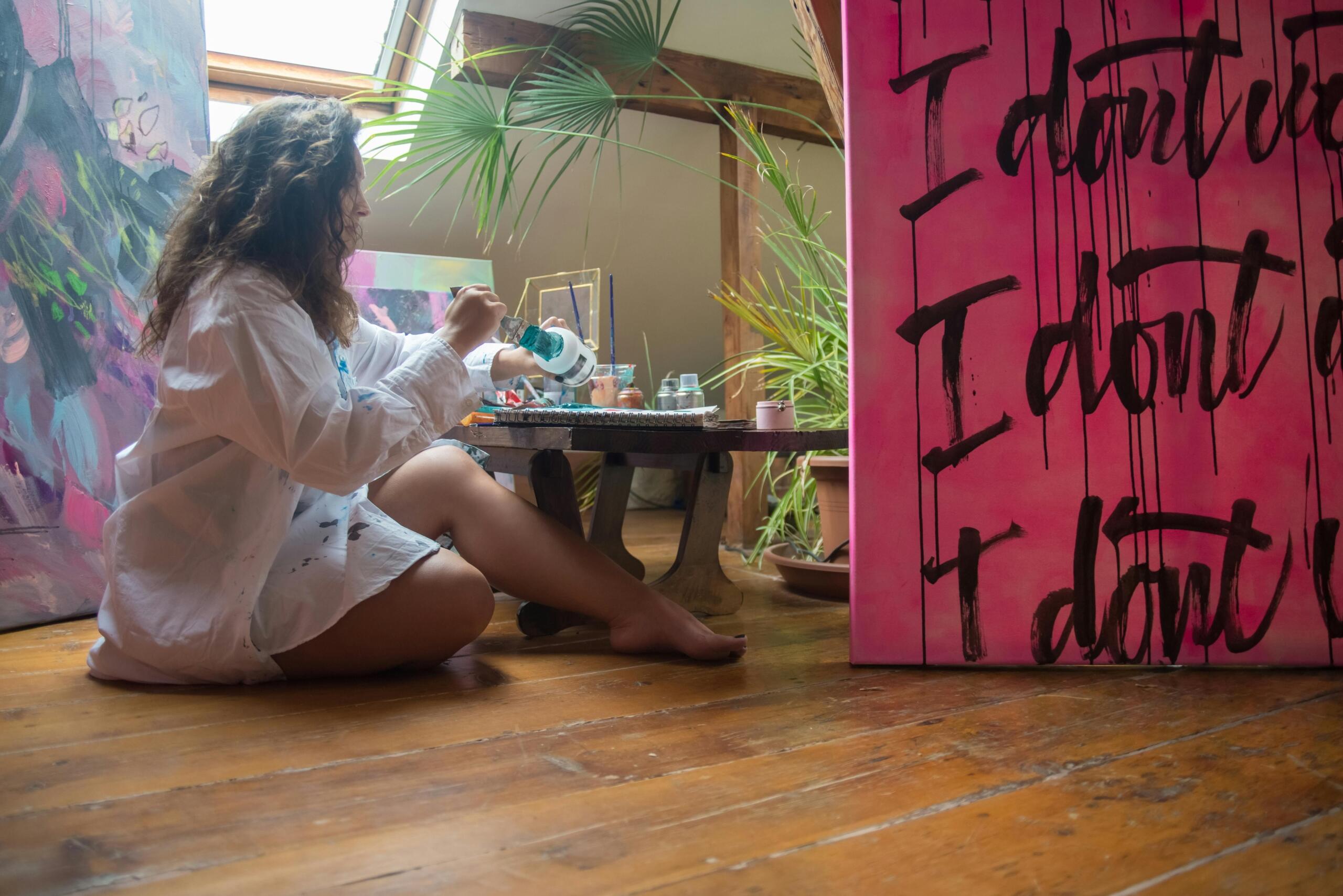 woman sitting on the floor amongst bold paintings on canvas cleaning her paintbrushes