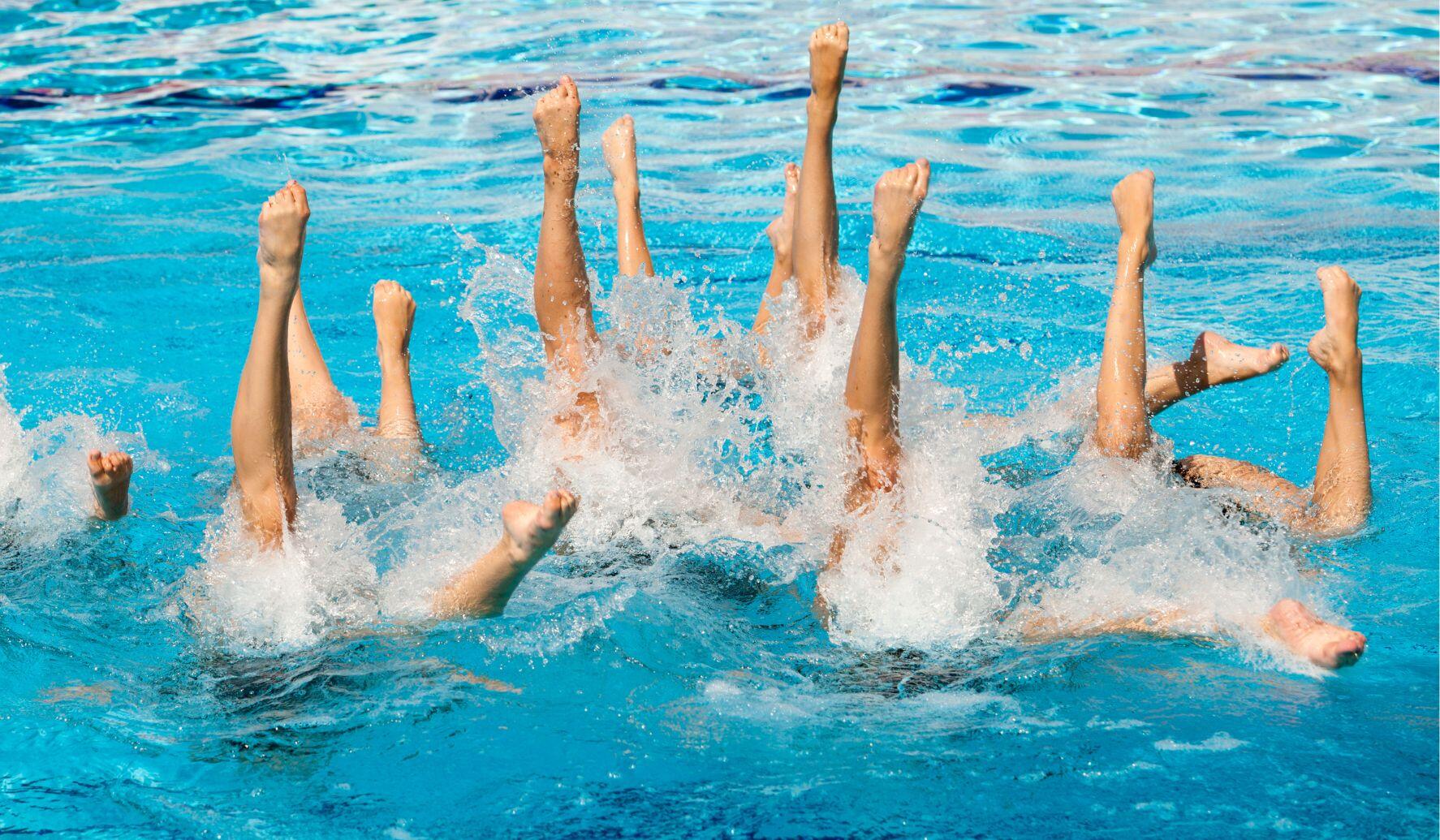 team of synchronised swimmers in a pool with their heads and torsos underwater and raising their legs in the air