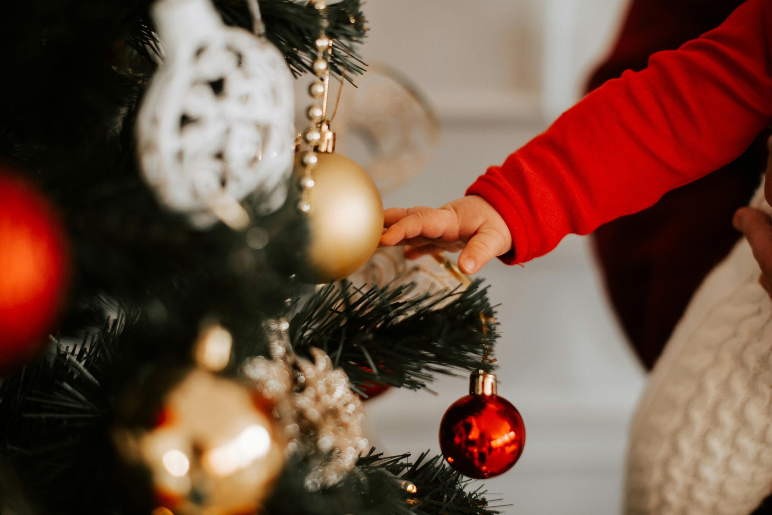 close up of baby's had reaching for Christmas bauble hanging on Christmas tree