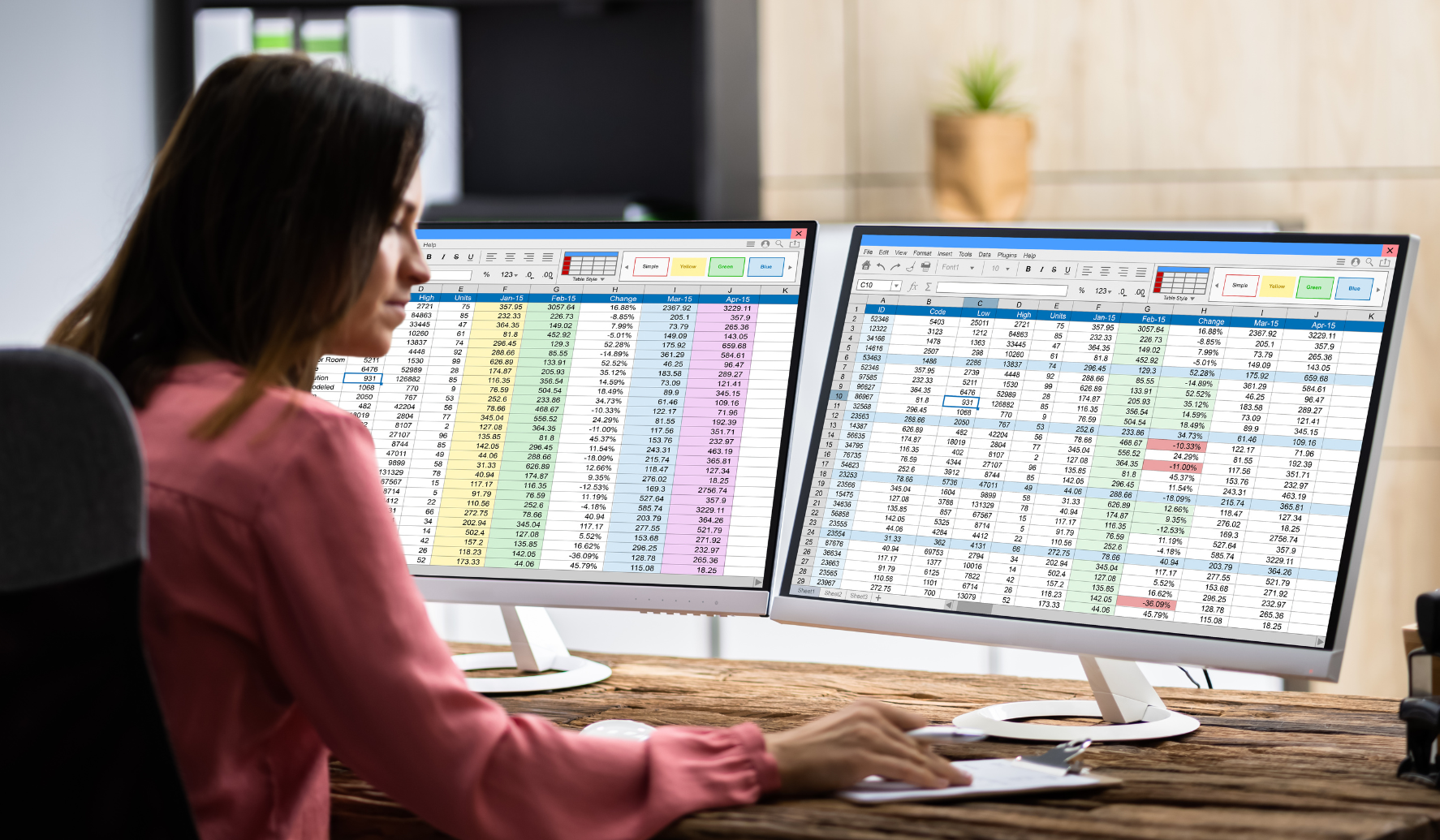 woman sitting at her desk using two desktop screens to review spreadsheets