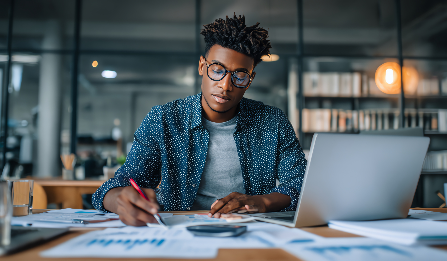 man sitting at desk using laptop and looking at printouts of graphs and data