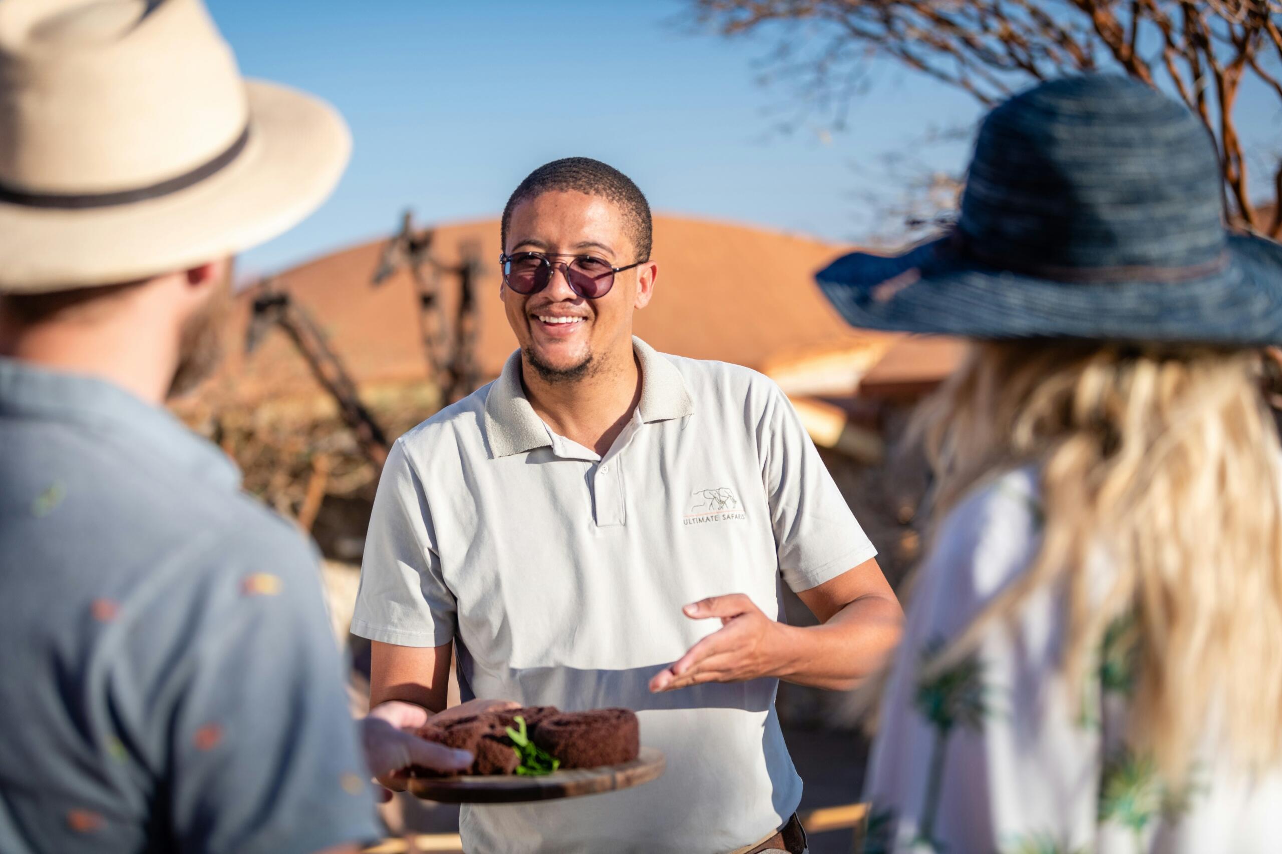 person offering two people food on a tray in the desert