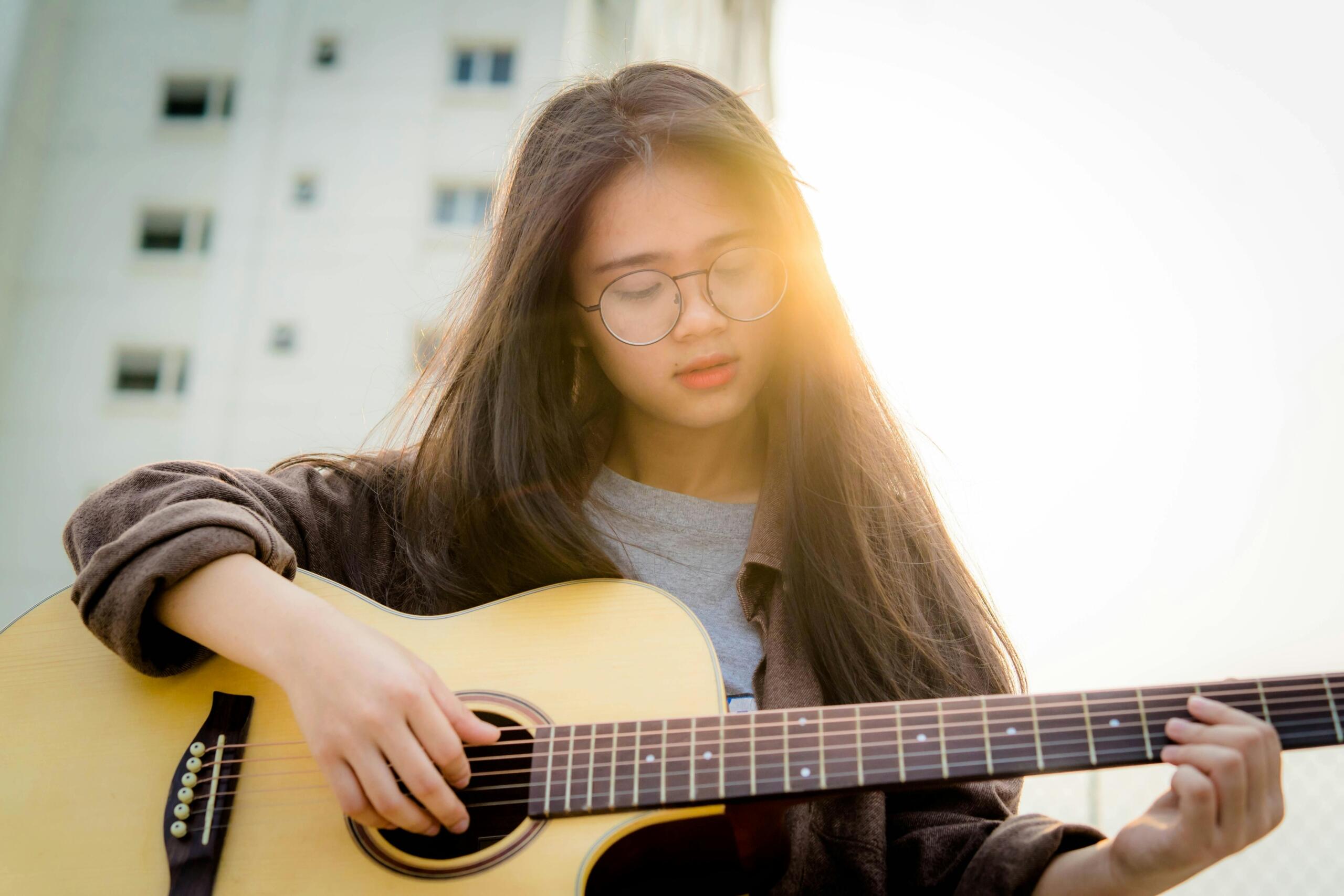 girl playing the guitar in front of a tall building