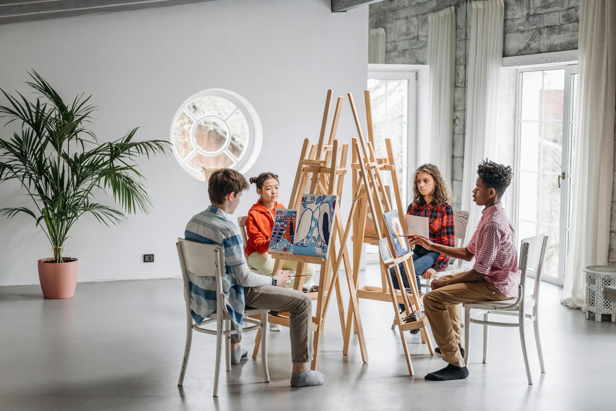 arts students painting on canvasses and seated behind easels arranged in a circle in art studio