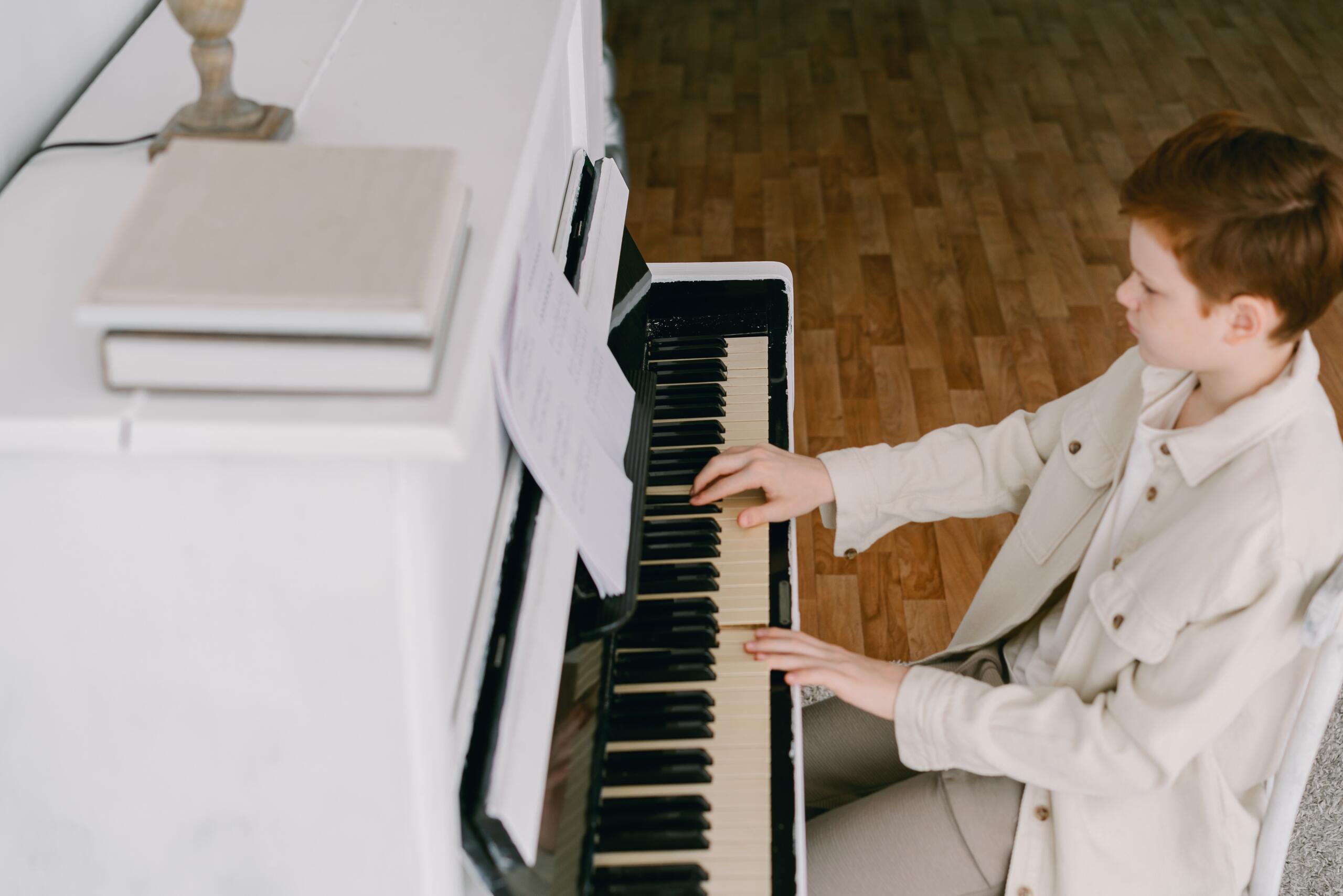 boy playing a white piano and reading sheet music