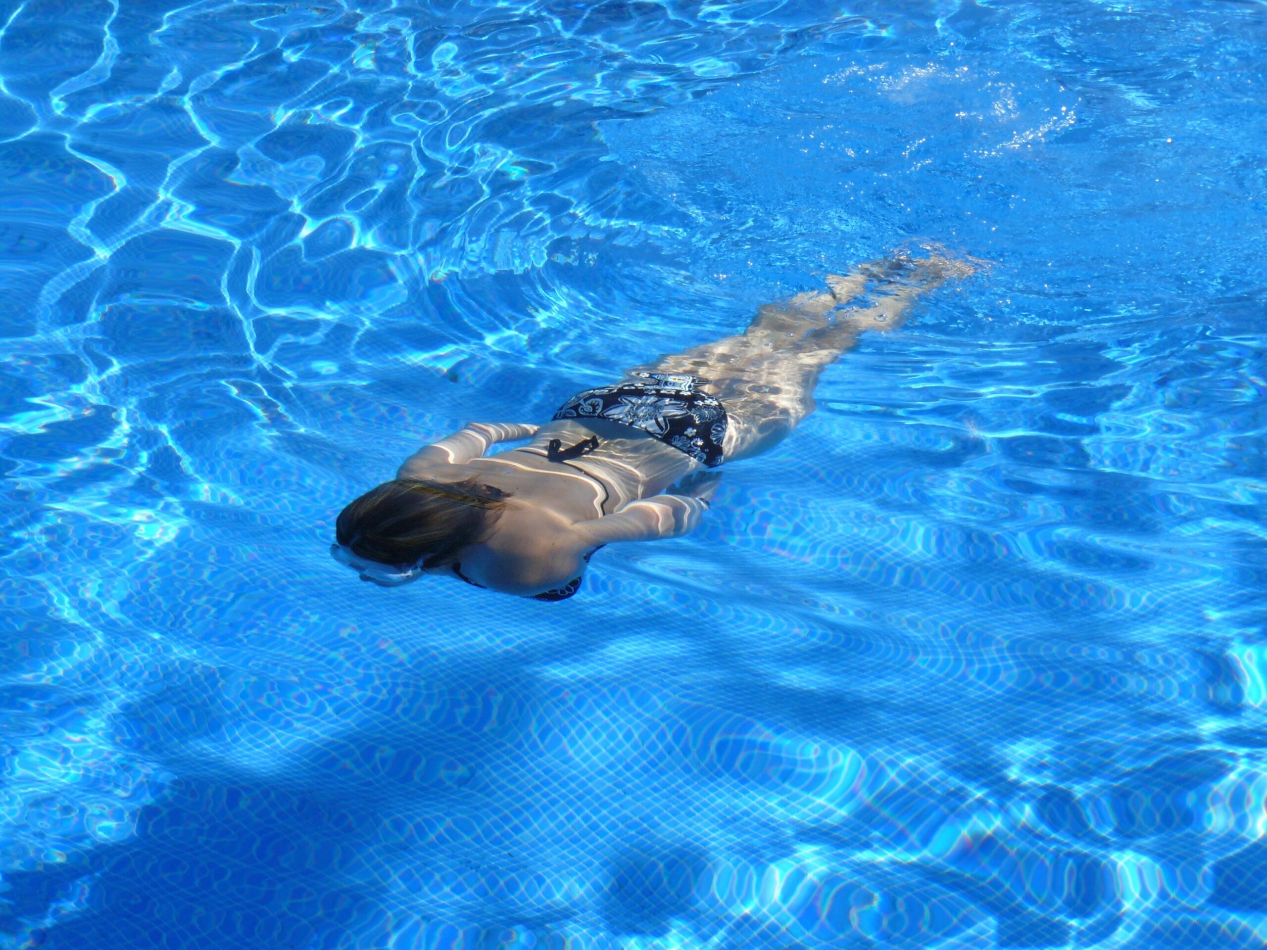 woman swimming underwater in swimming pool wearing goggles