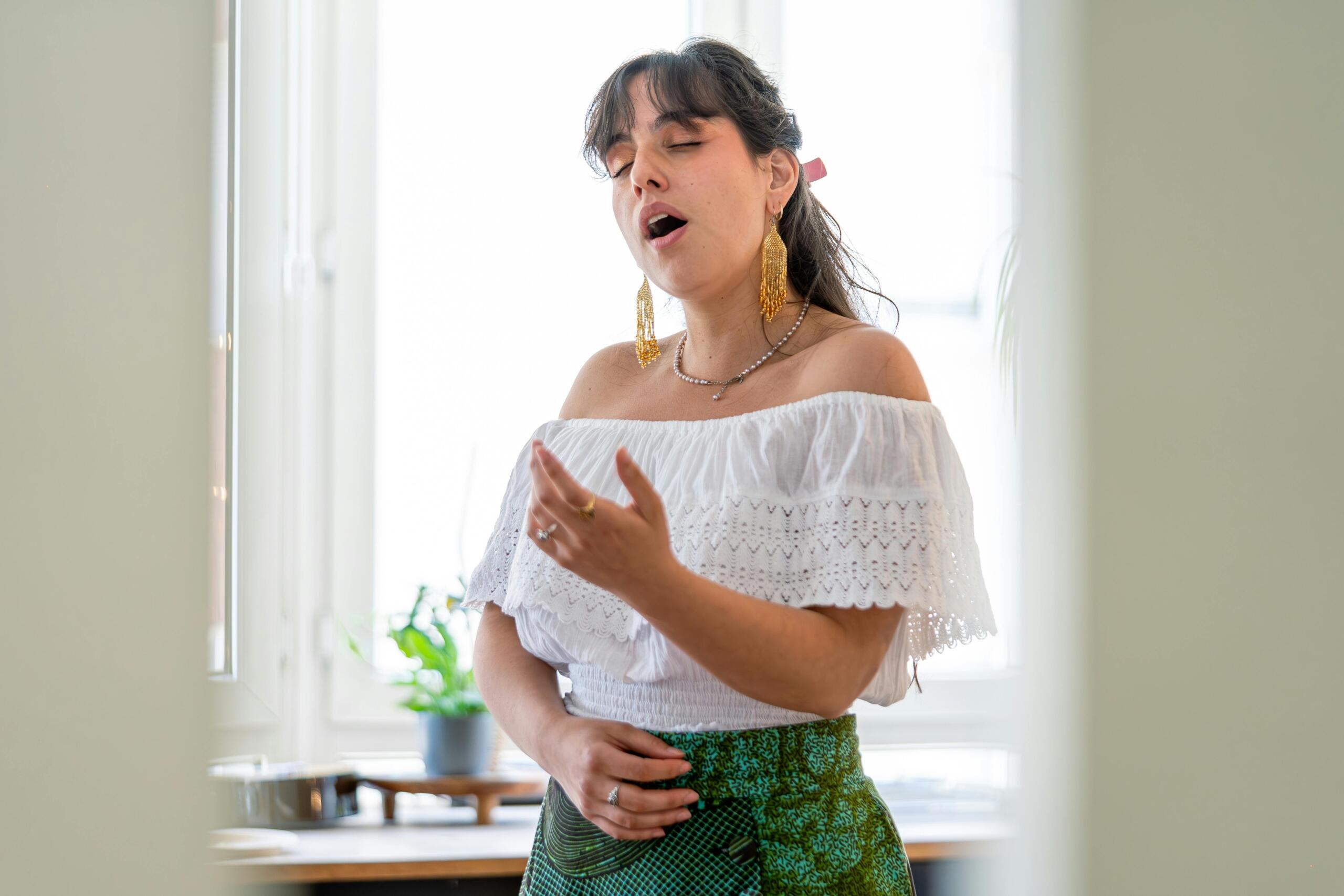 woman standing in a room and singing with her eyes closed while reaching a hand in front of her