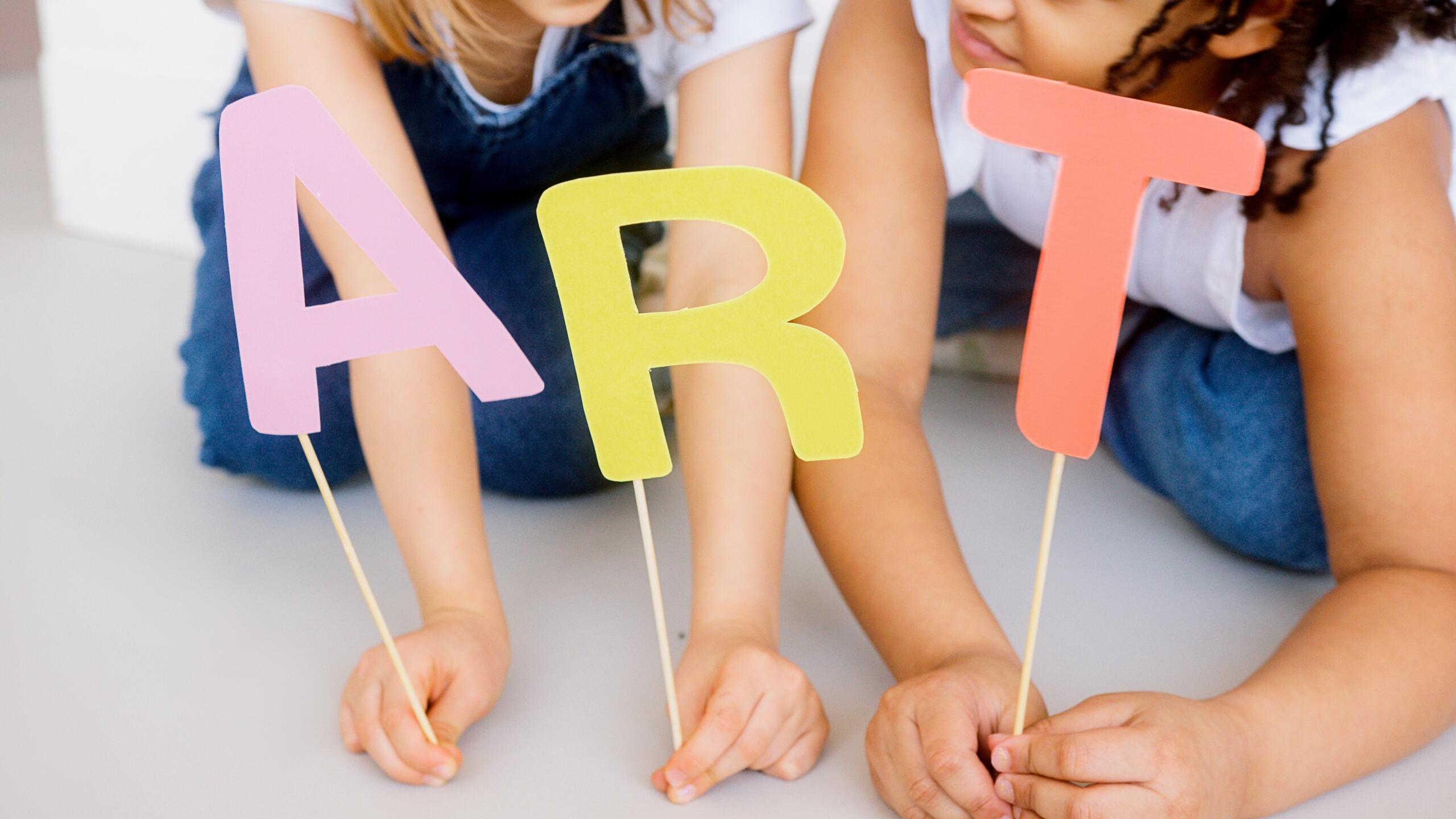 two young children holding letters that spell out the word art glued to sticks