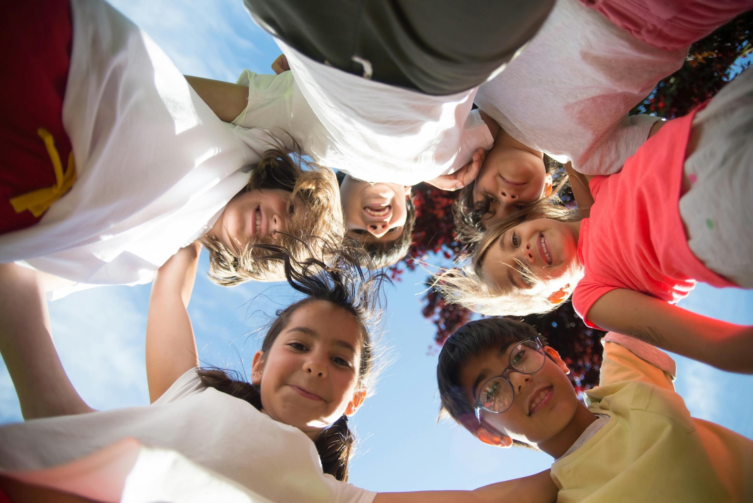 image of children standing in a circle with their arms around each others' shoulders taken from the ground