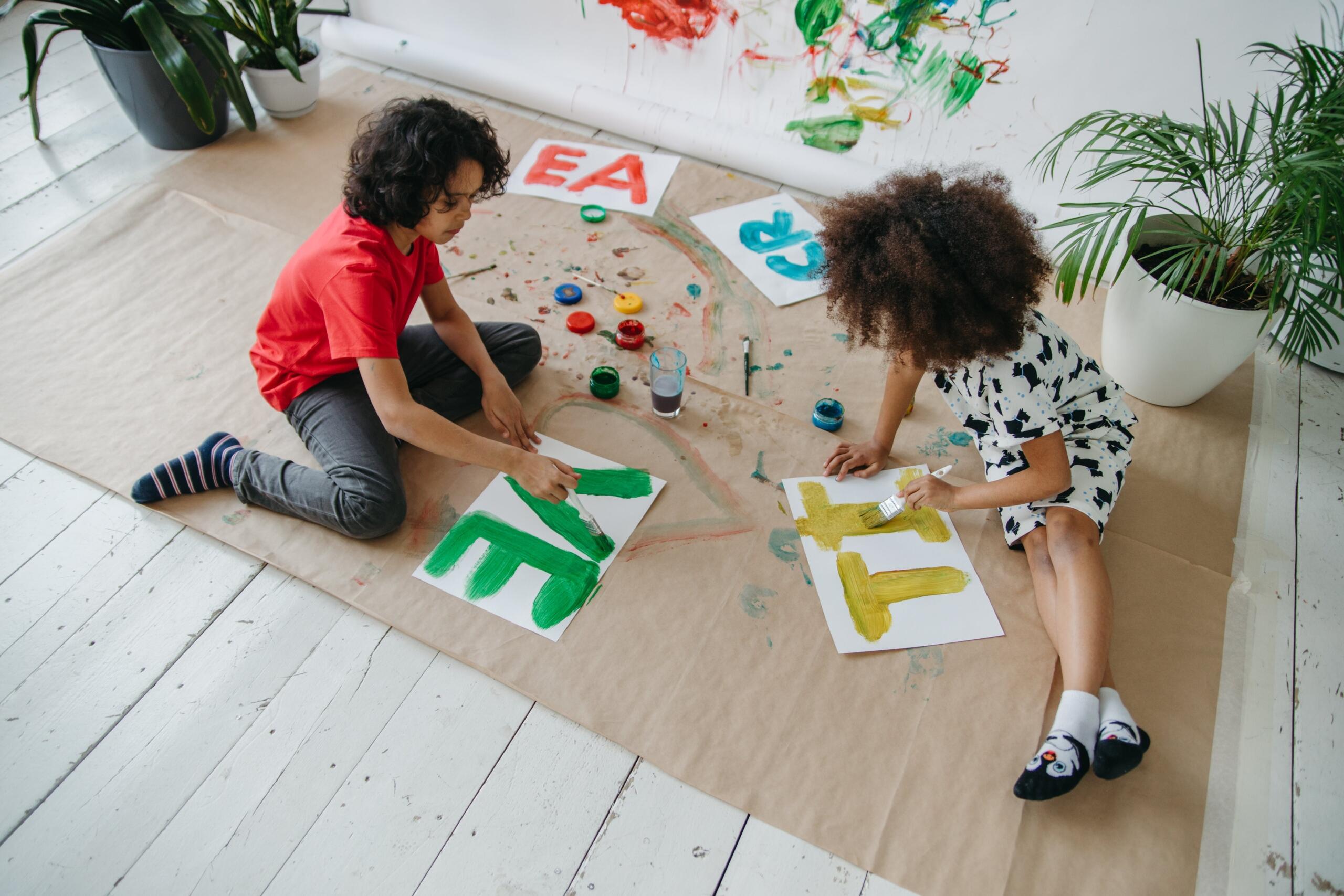 two children sitting on a sheet of brown paper on the floor painting on paper