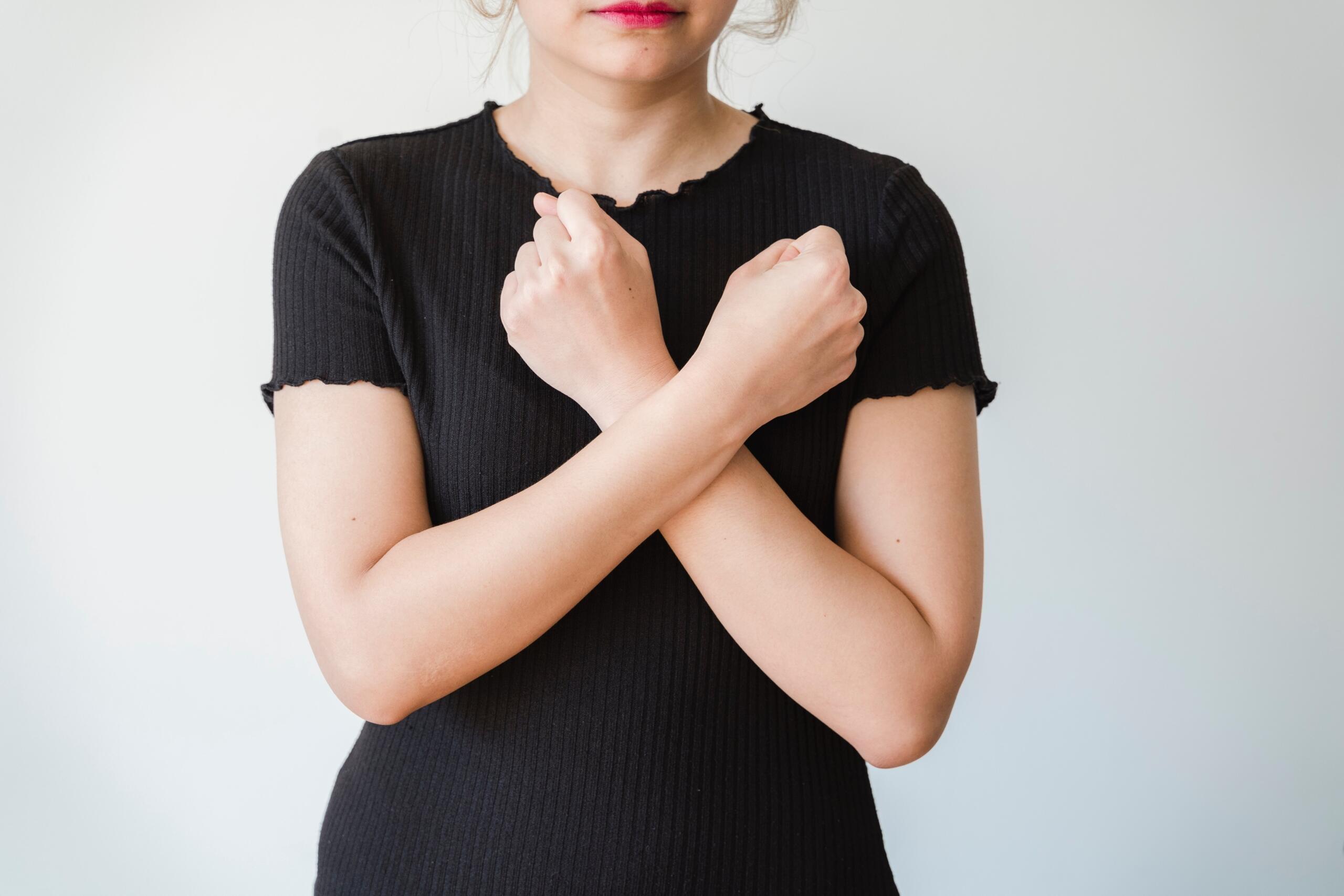 woman making sign language gesture crossing arms across body diagonally with elbows bent