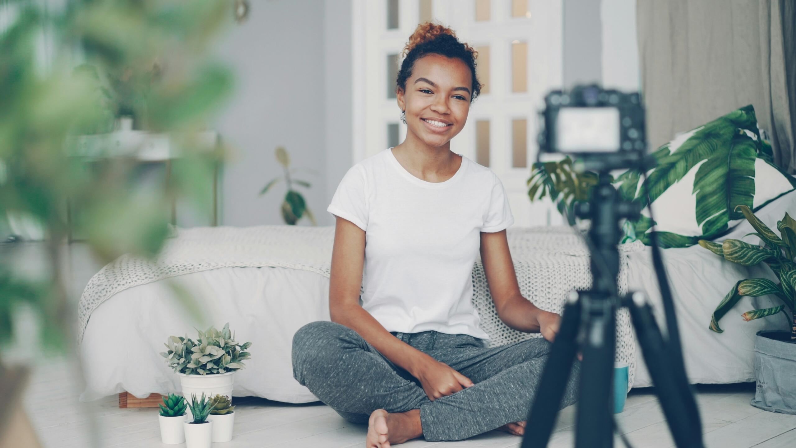 girl sitting on the floor smiling at a camera balanced on a tripod