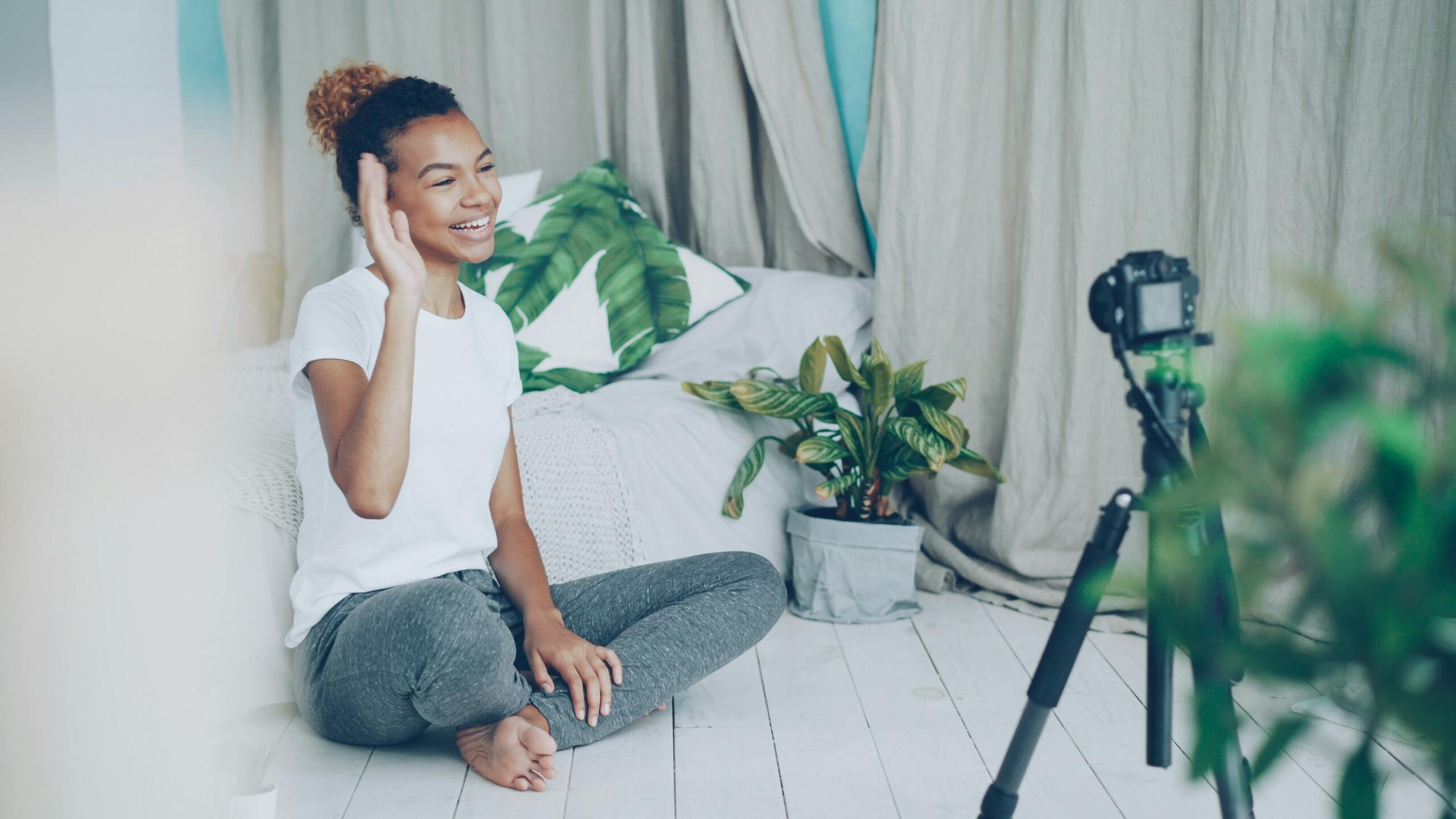 girl sitting on the floor waving at a camera balanced on a tripod
