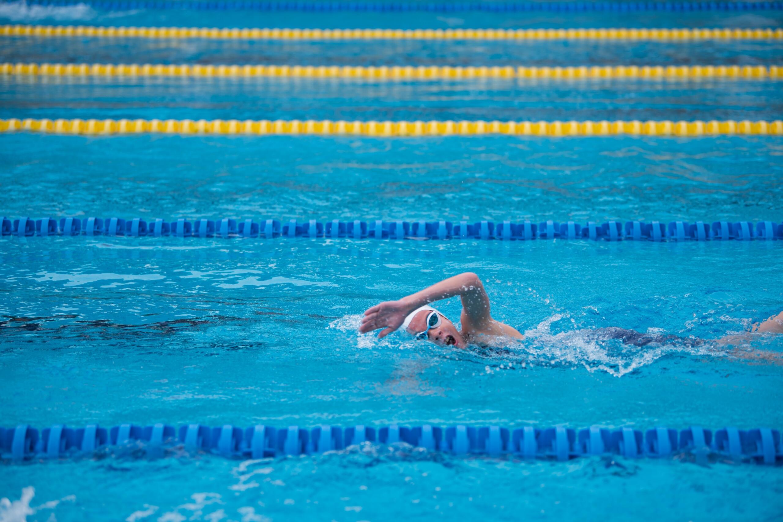 person wearing swimming goggles and swim cap swimming in lanes in a pool