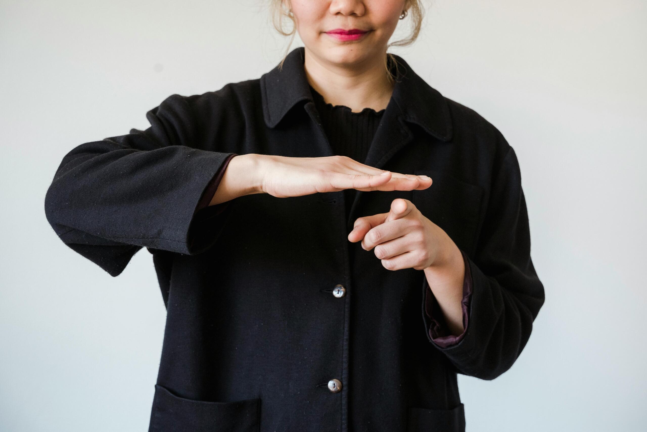 woman making sign language gesture pointing the index finger of left hand and placing right hand flat on top of left hand