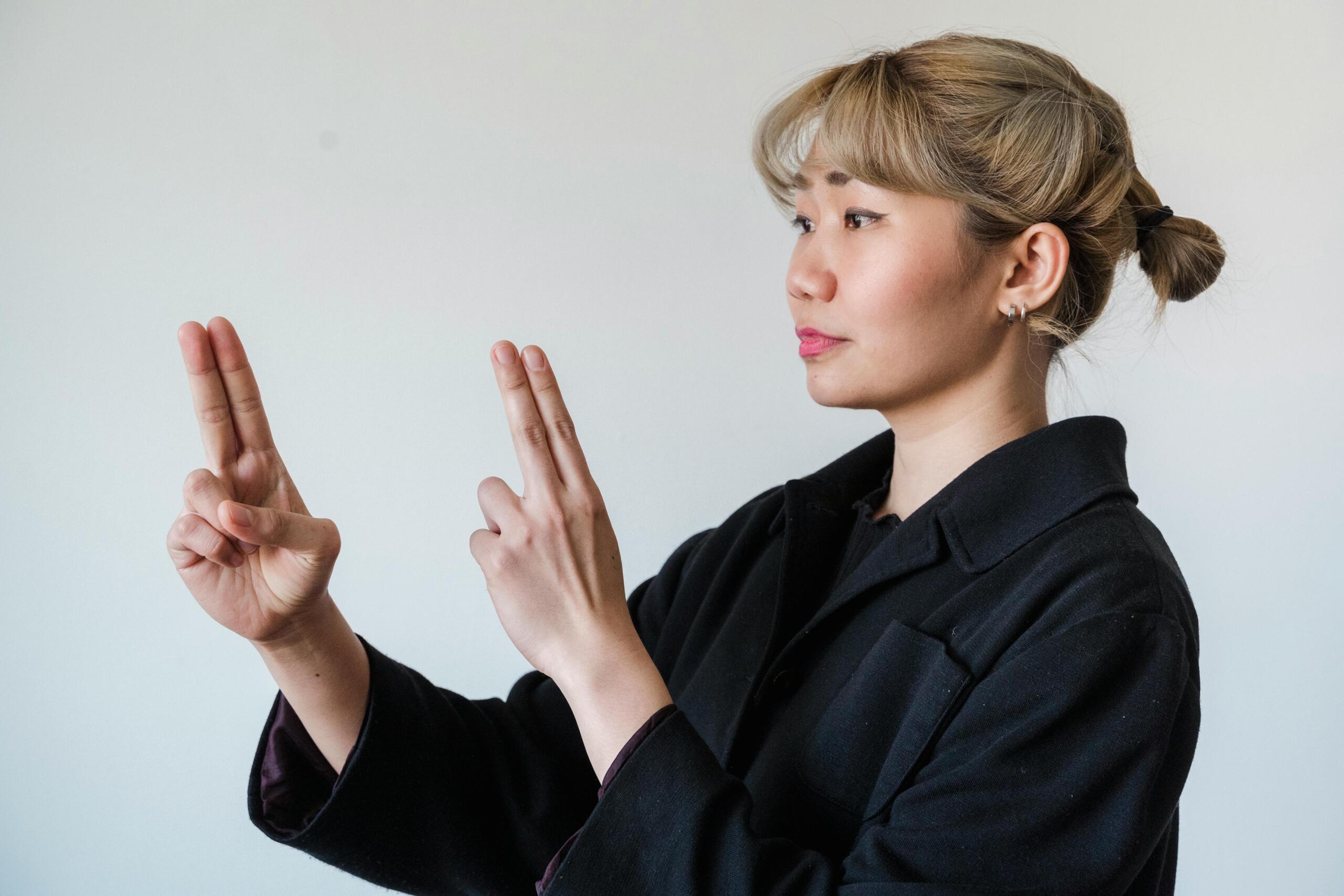 woman making sign language gesture pointing the index and middle fingers of both hands upwards