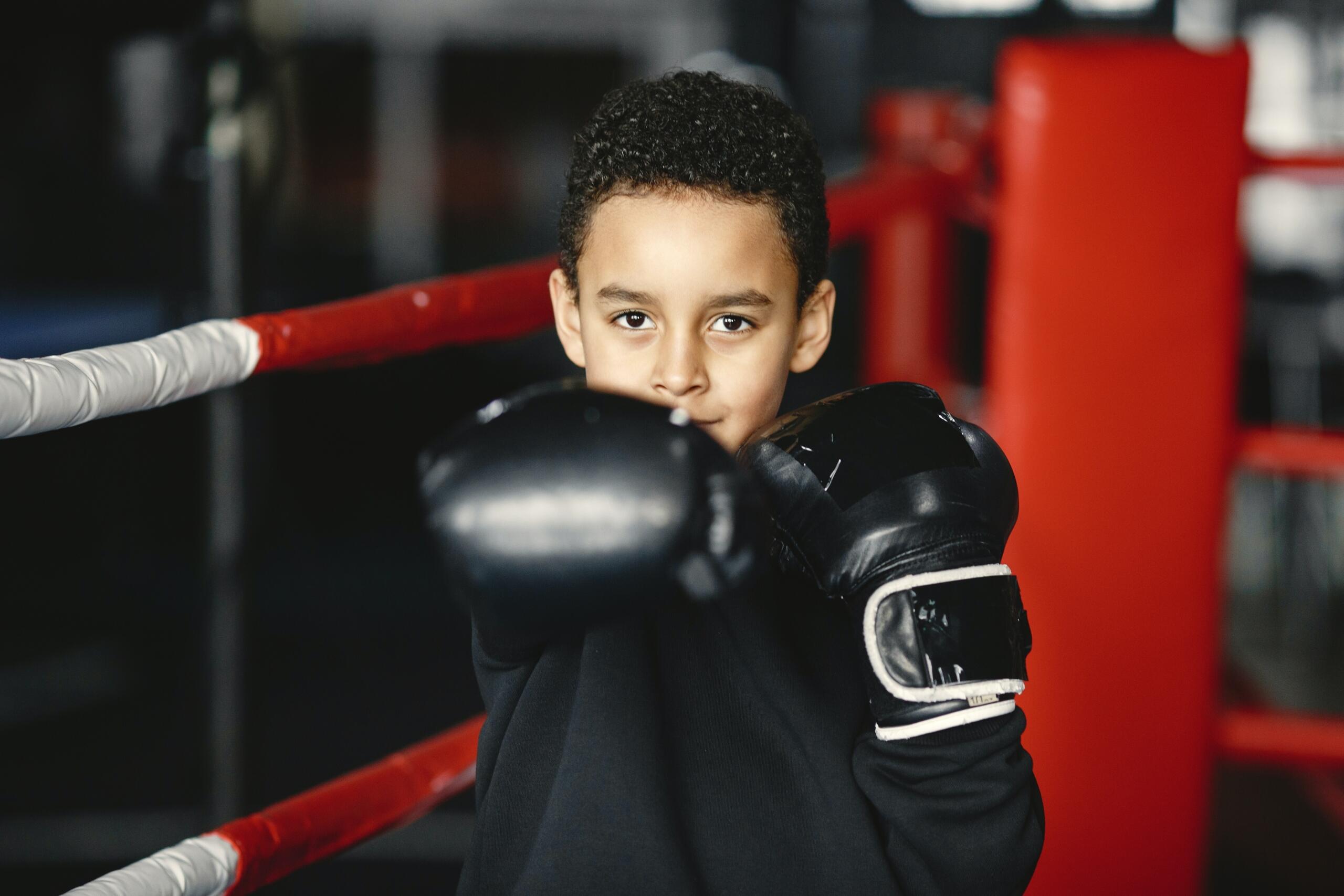 smiling boy in a boxing ring wearing boxing gloves and punching towards the camera