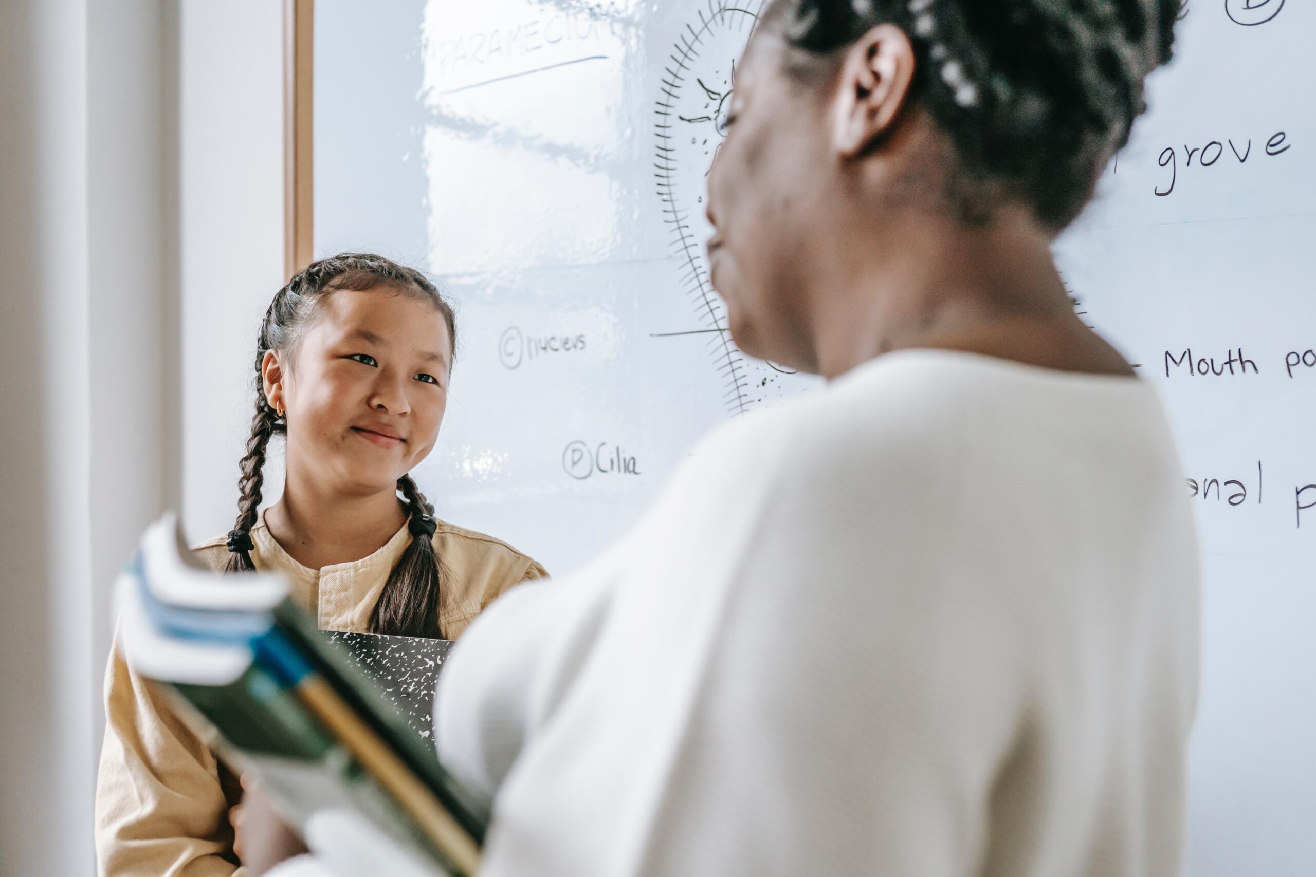 smiling student talking to teacher in front of white board displaying a drawingof a mitochondria