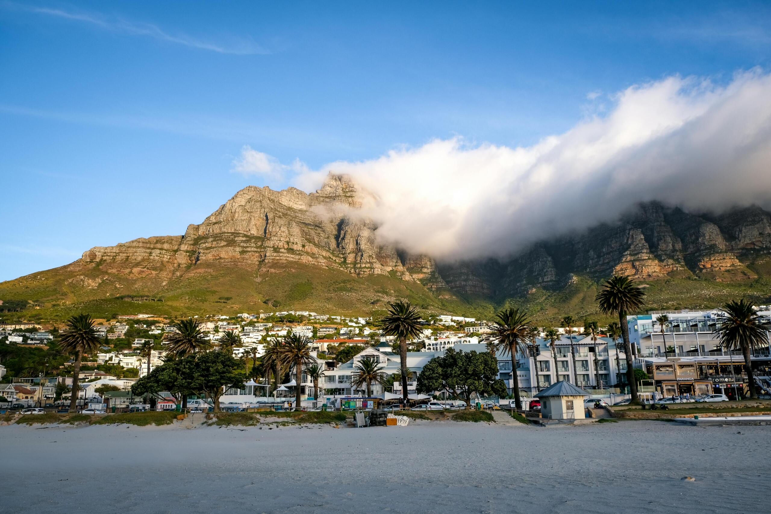 image of clouds rolling over table mountain seen from the white sands of camps bay beach