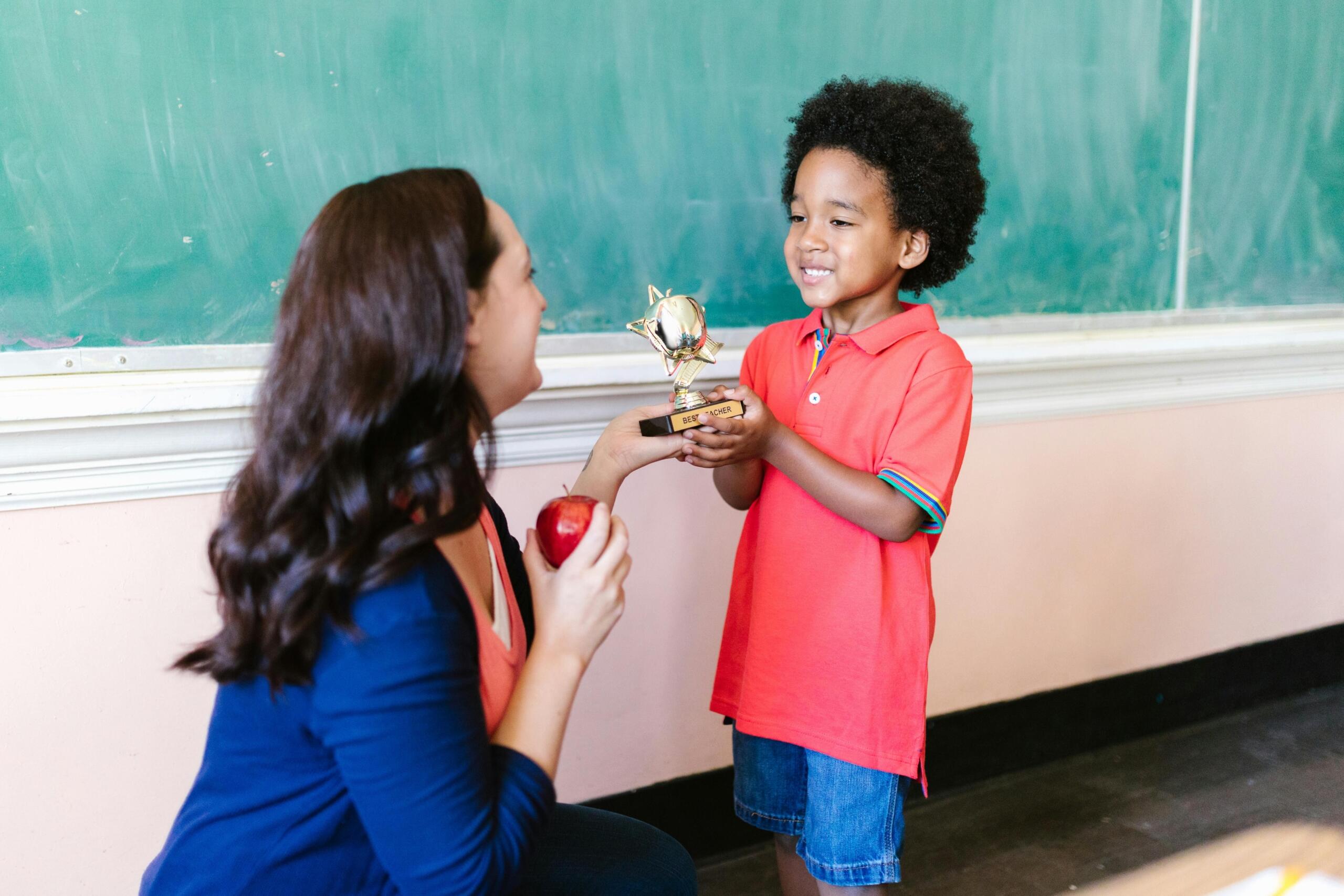 young boy receiving a trophy from his teacher in front of the classroom