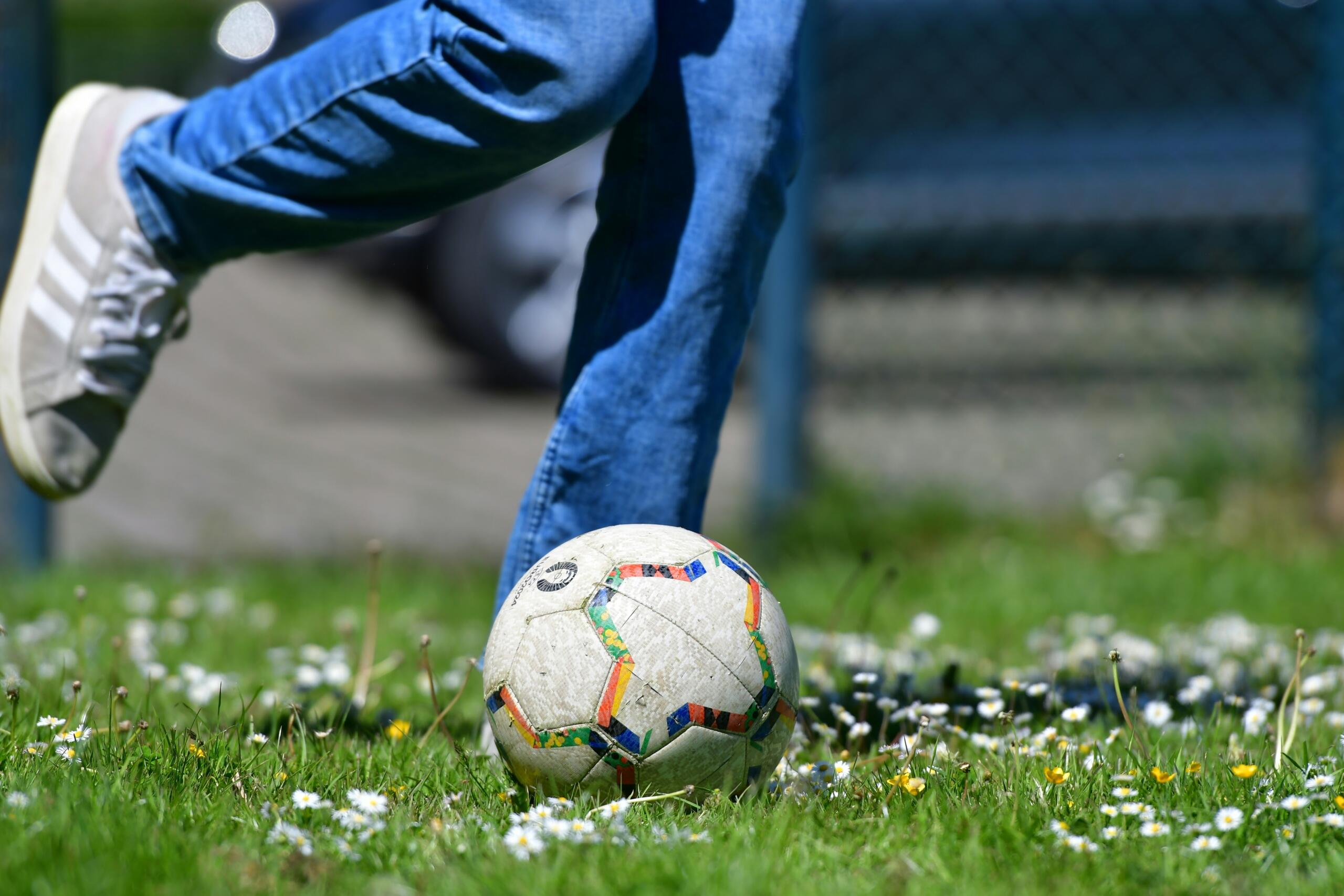 image of the legs of a child about to kick a soccer ball on grass