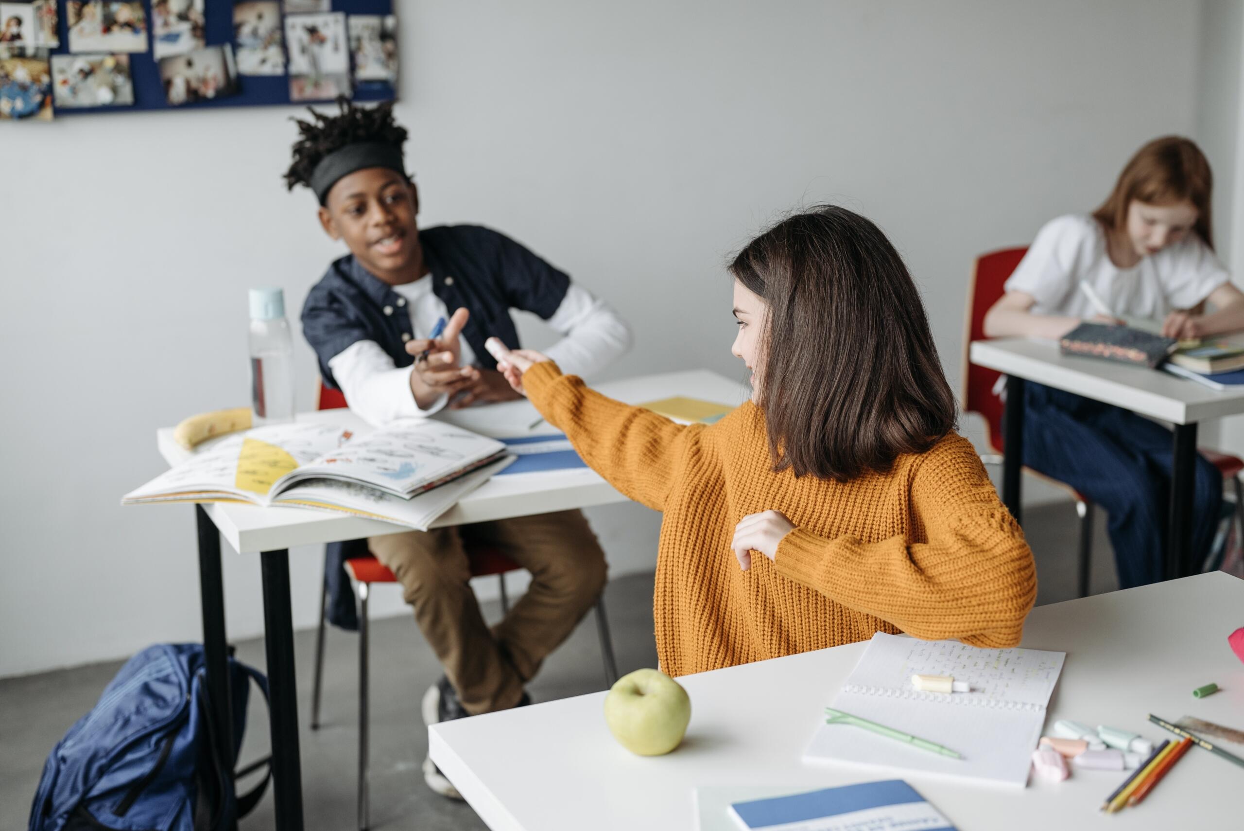 school girl passing an item to the school boy seated at the table behind her