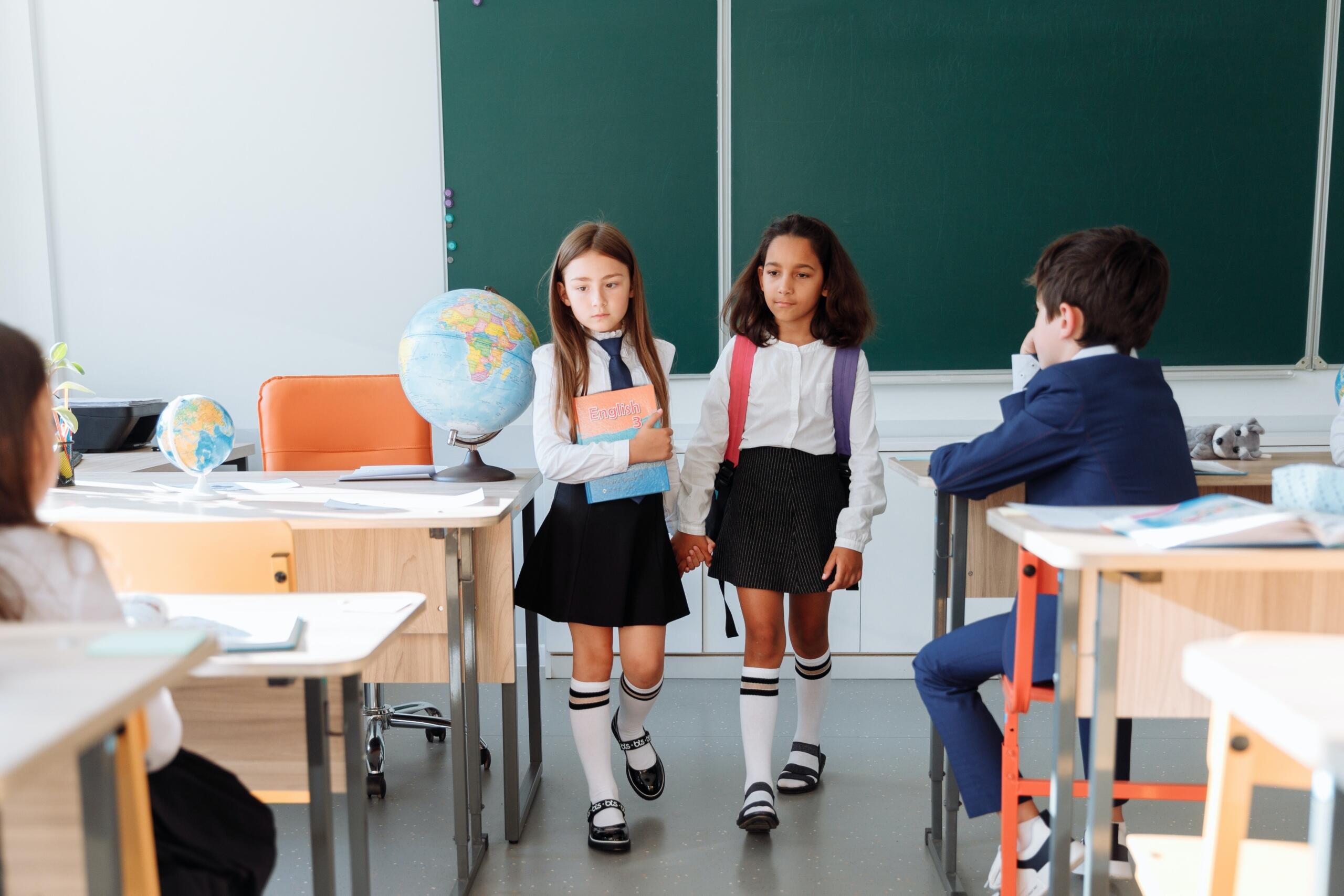 two schoolgirls in school uniform walking down the passage in a classroom