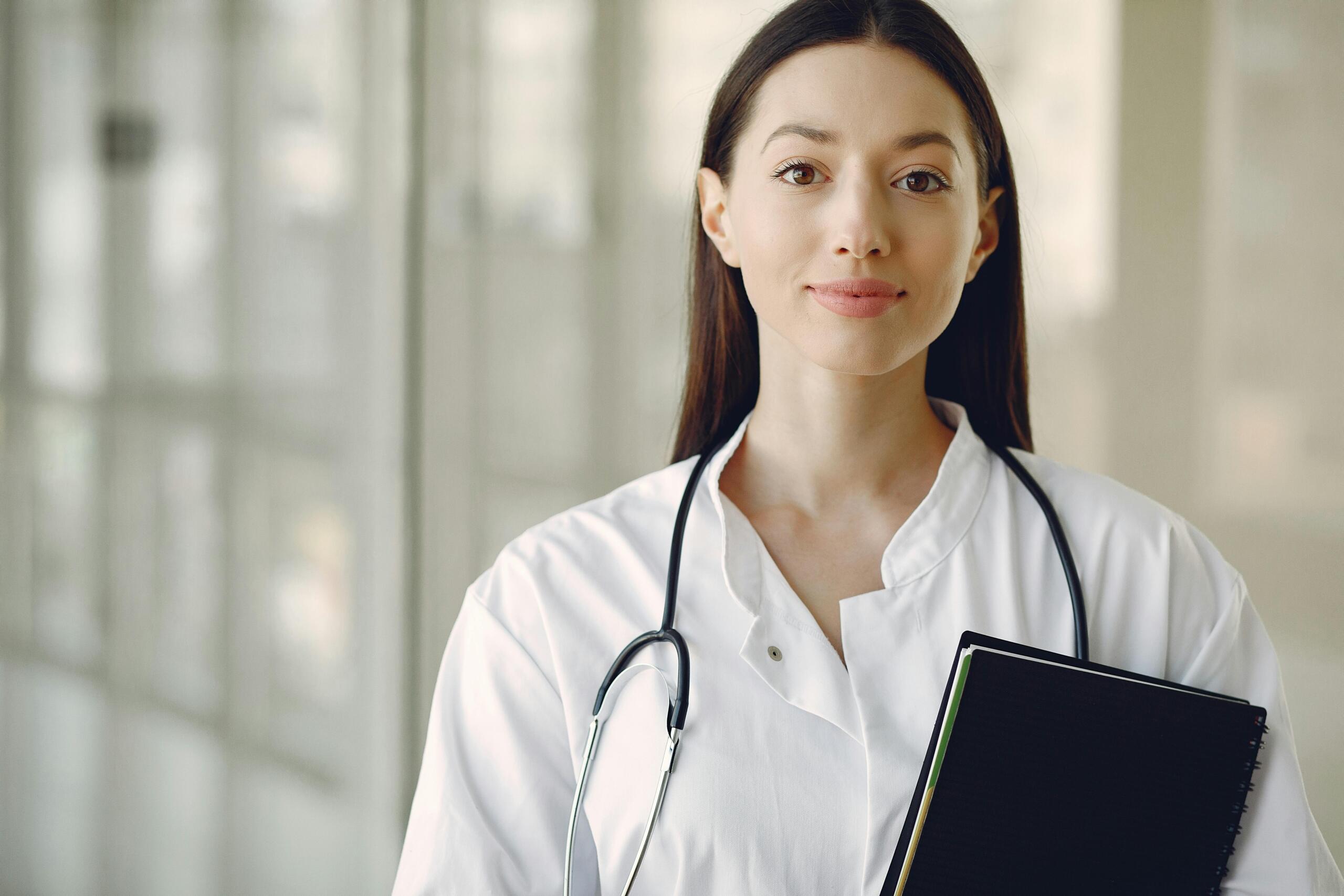 doctor in lab coat with stethoscope around her neck and carrying notebook