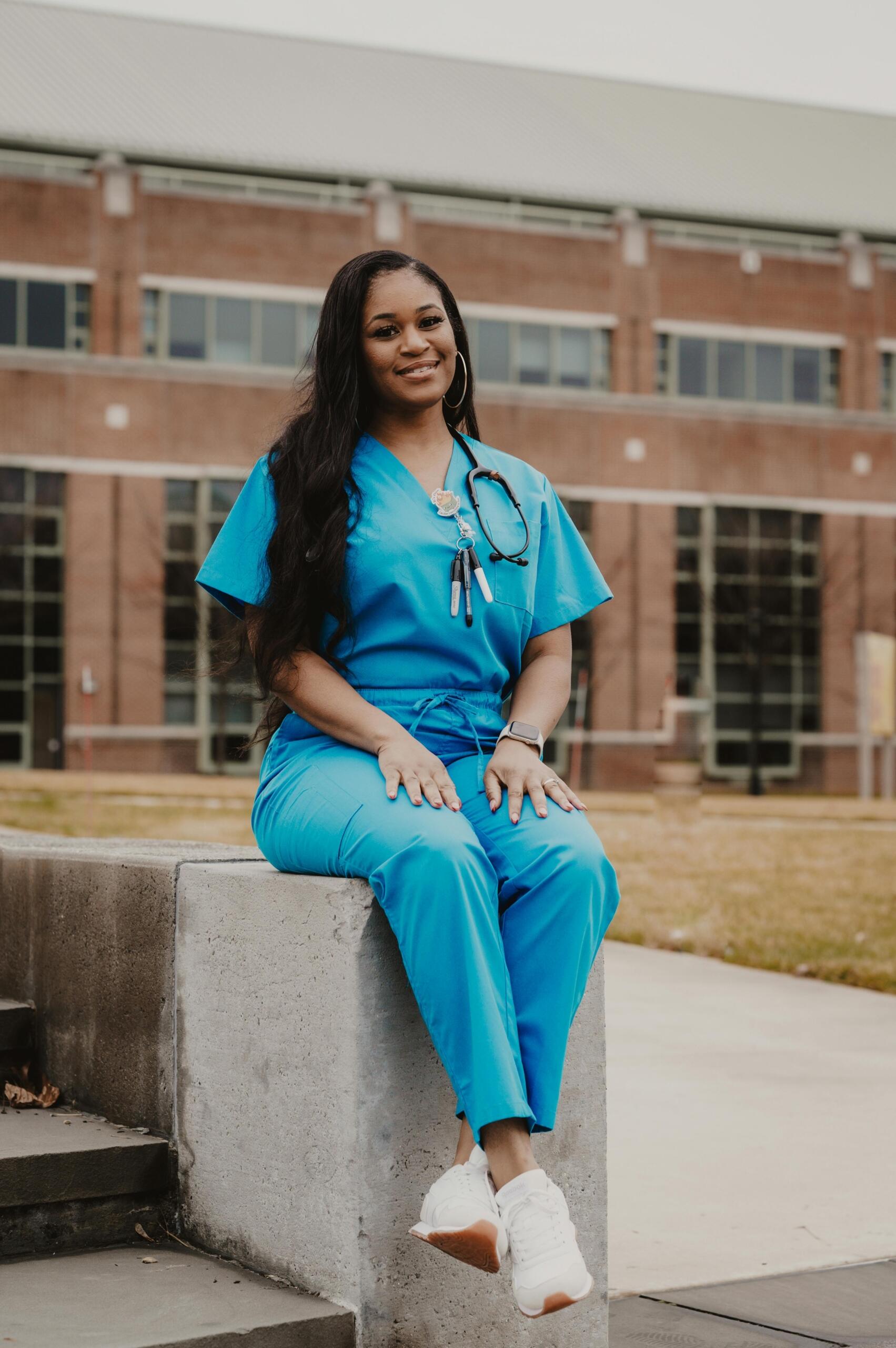 smiling doctor in blue scrubs sitting outside hospital
