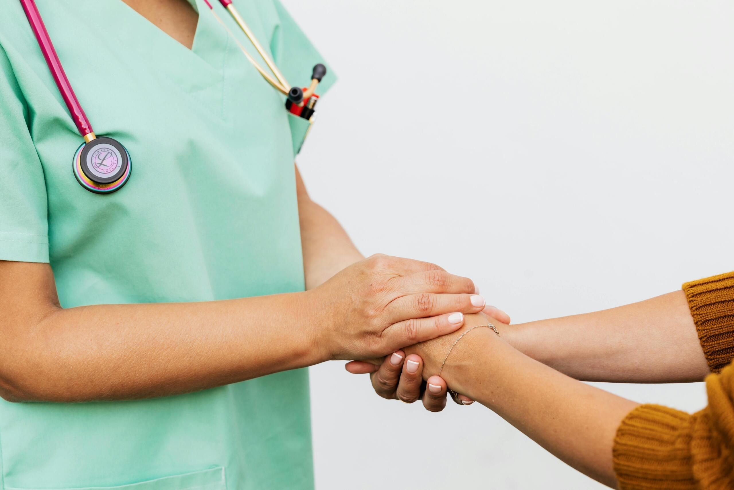doctor in scrubs with stethoscope around her neck holding the hand of a patient