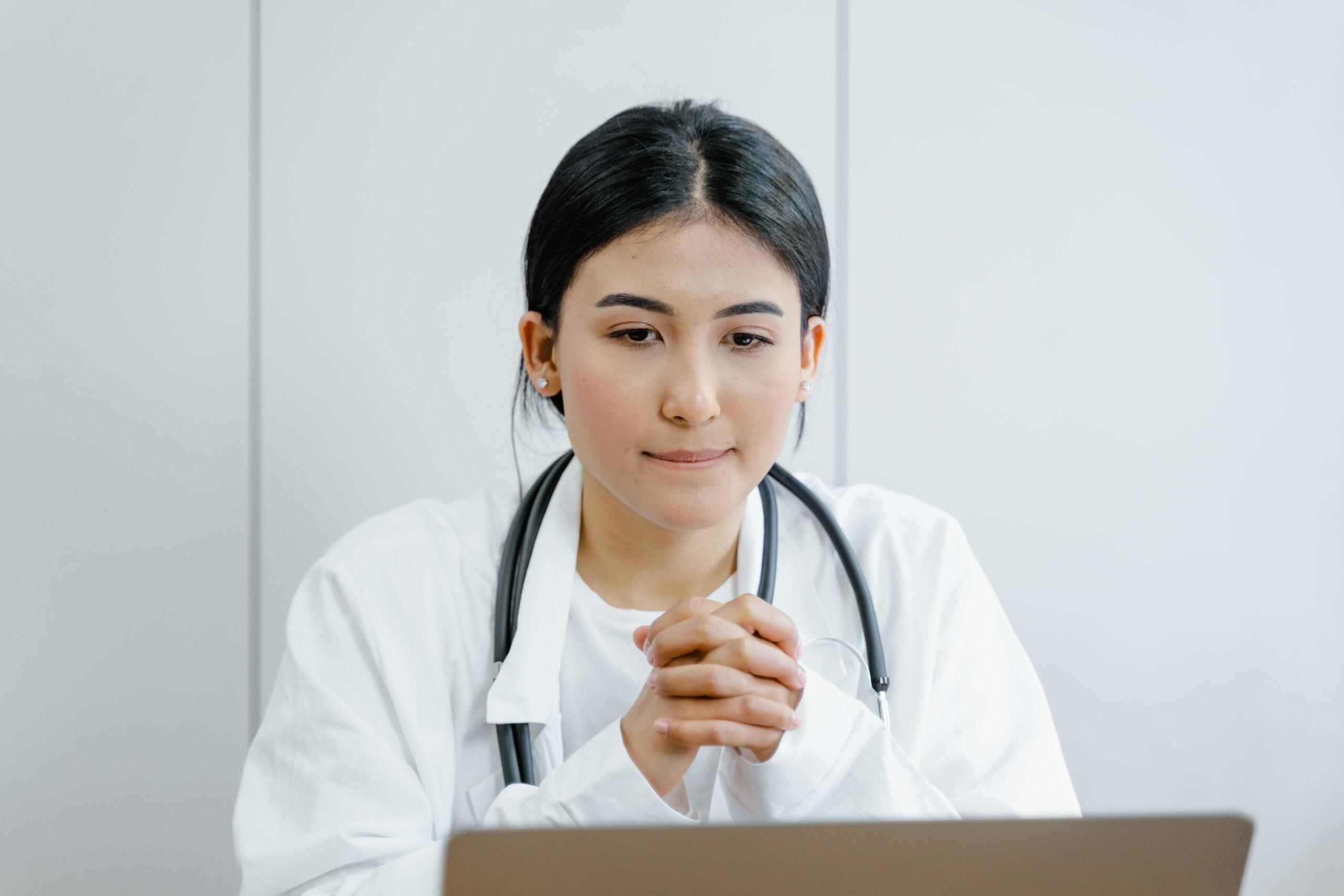 doctor in white lab coat with stethoscope around her neck sitting behind a desk