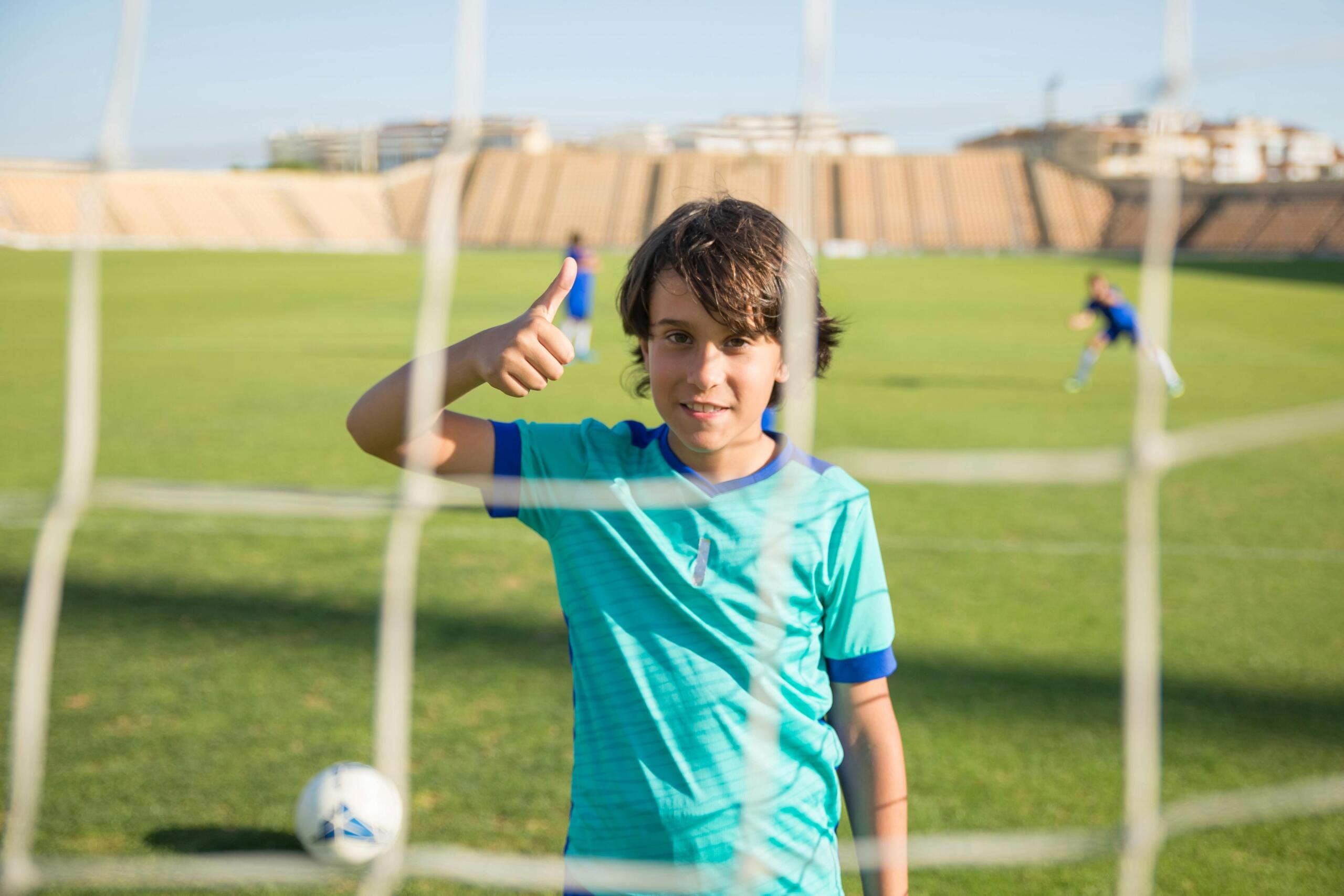 young boy on the soccer pitch standing in goal and giving a thubs up