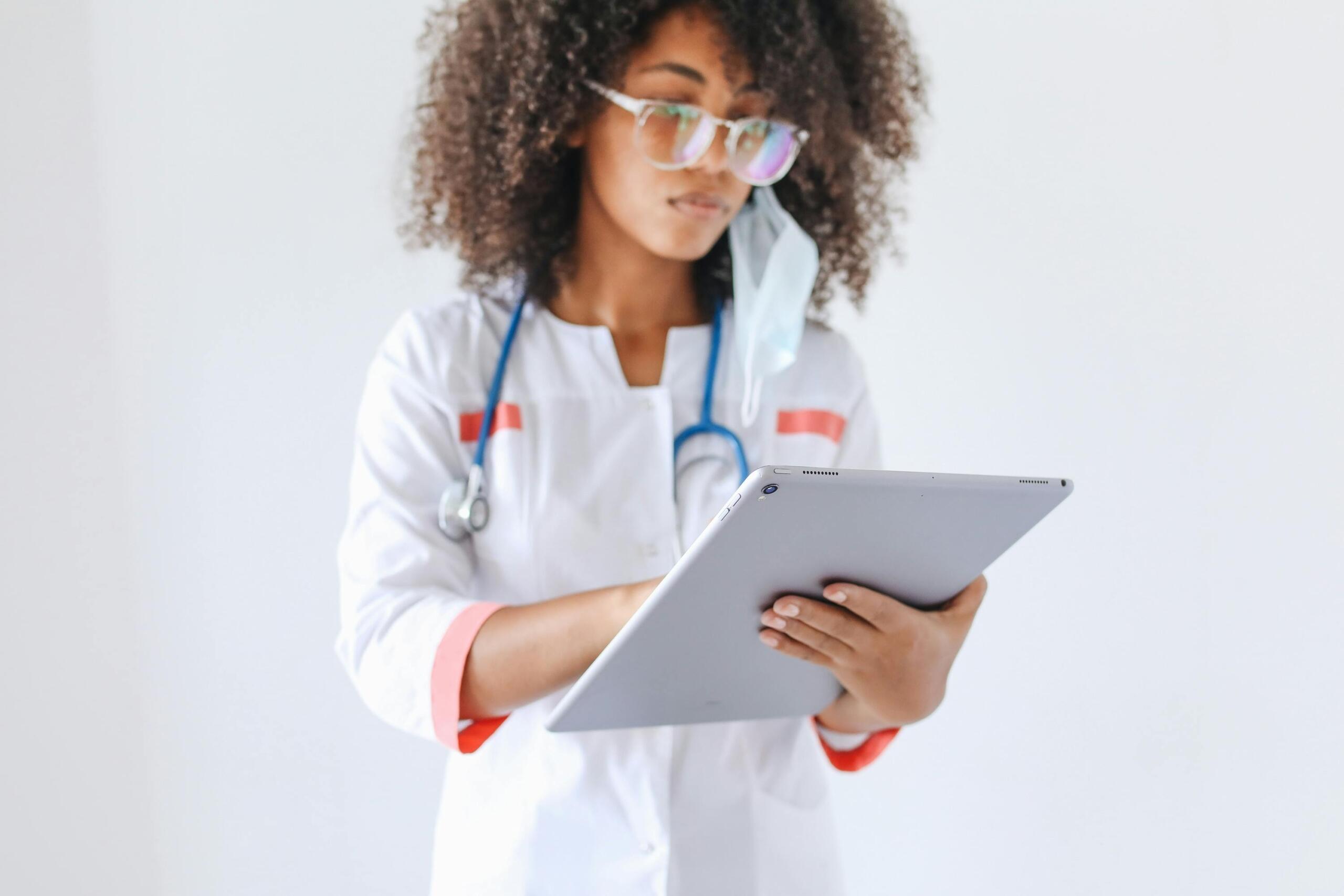 doctor in white coat with stethoscope around her neck wearing face mask and using ipad
