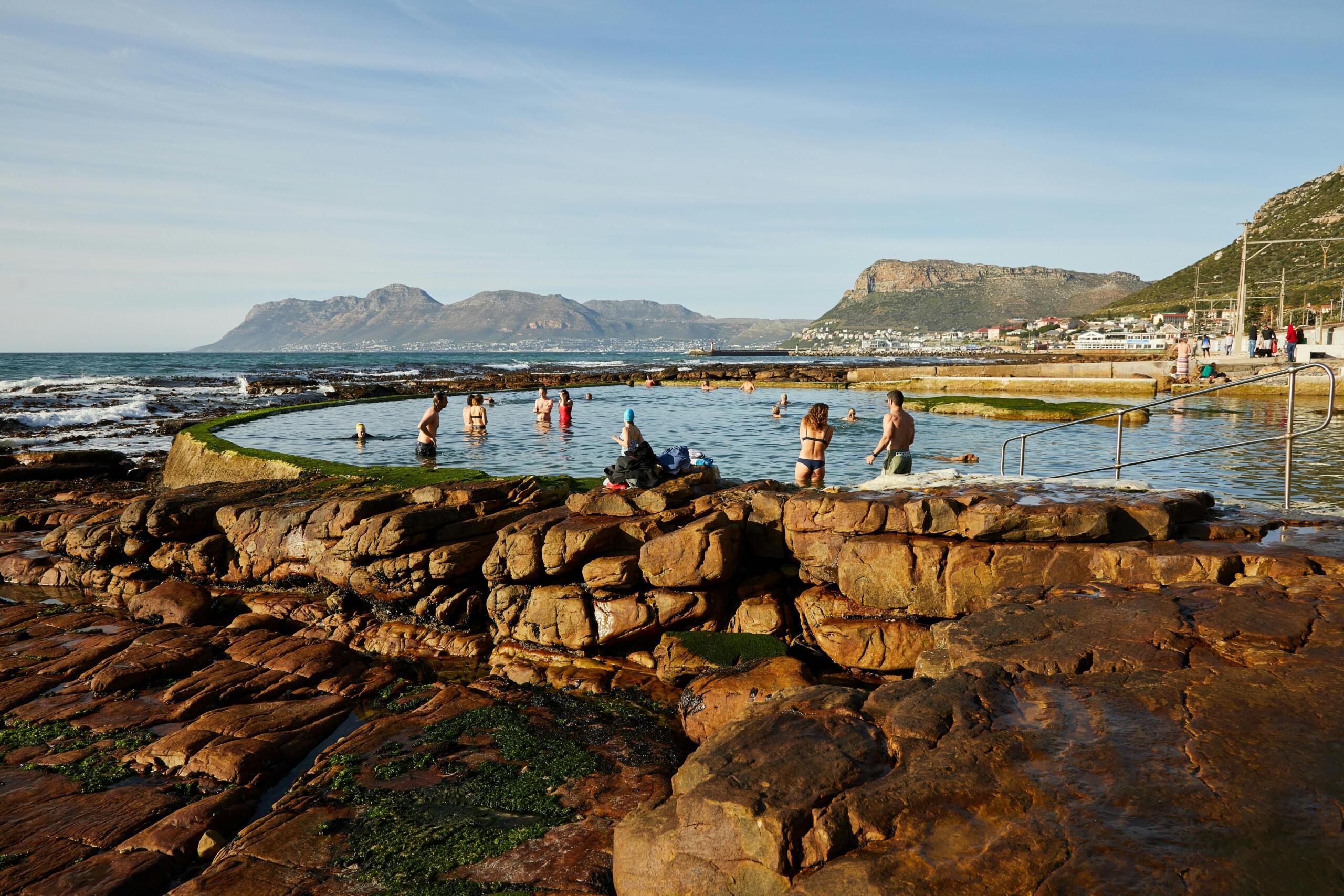 people standing in a tidal pool in the ocean surrounded by rocks on Cape Town's False Bay coast