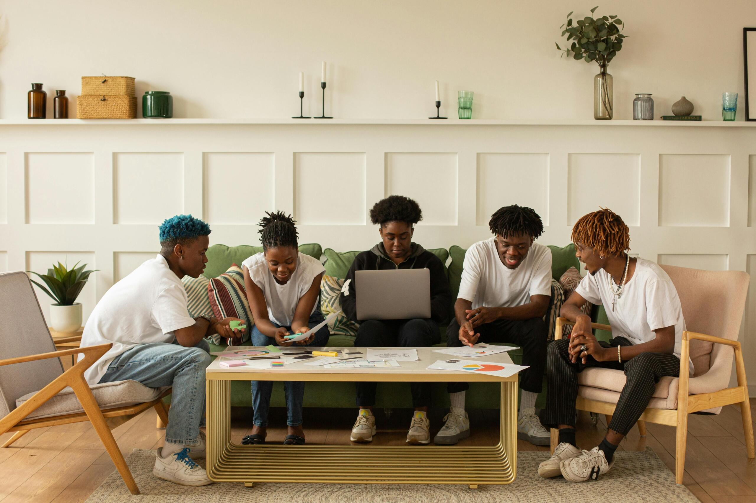 a group of students sitting on a couch and chairs around a table working on an assignment together