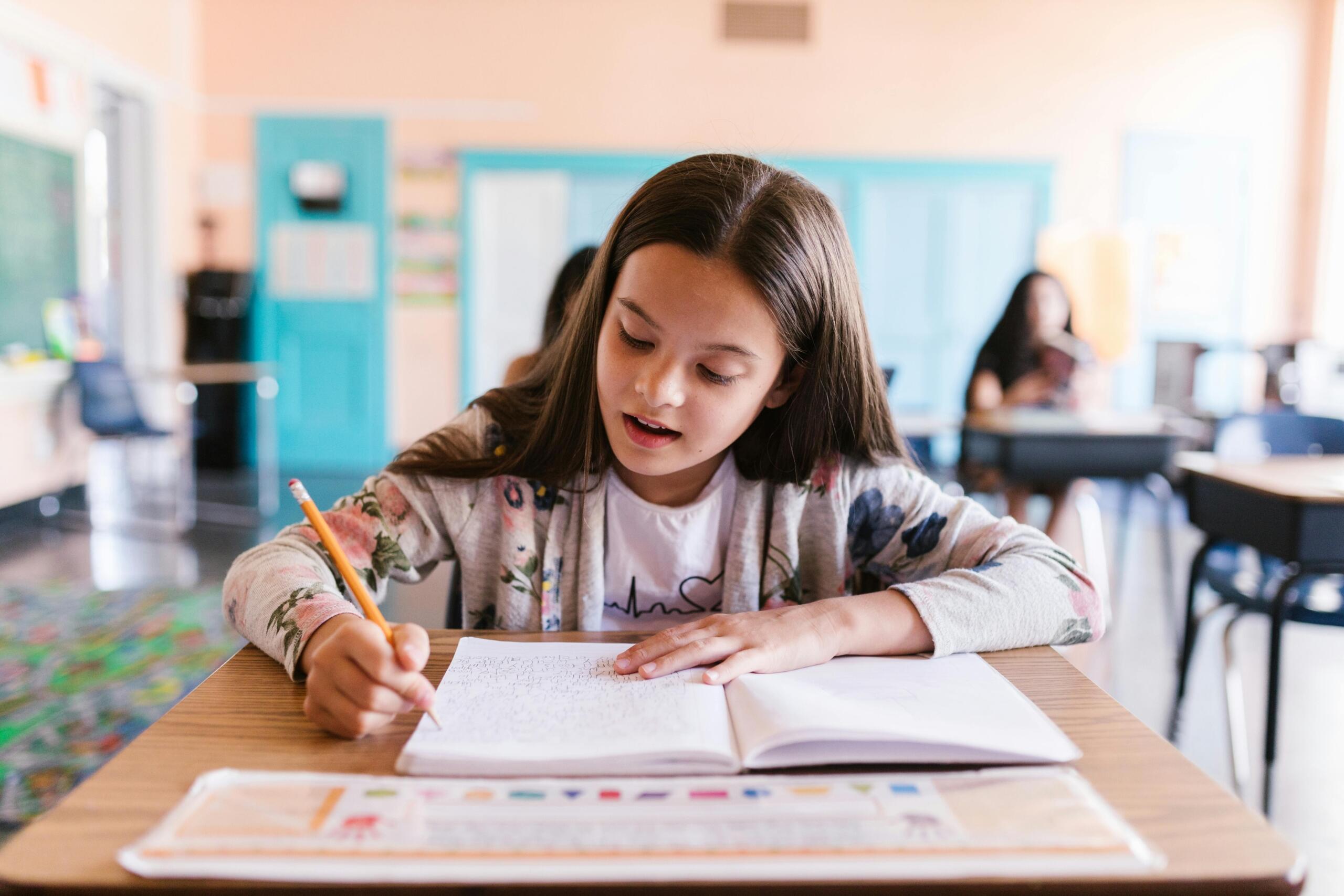 focus on one student sitting at desk in classroom writing in notebook