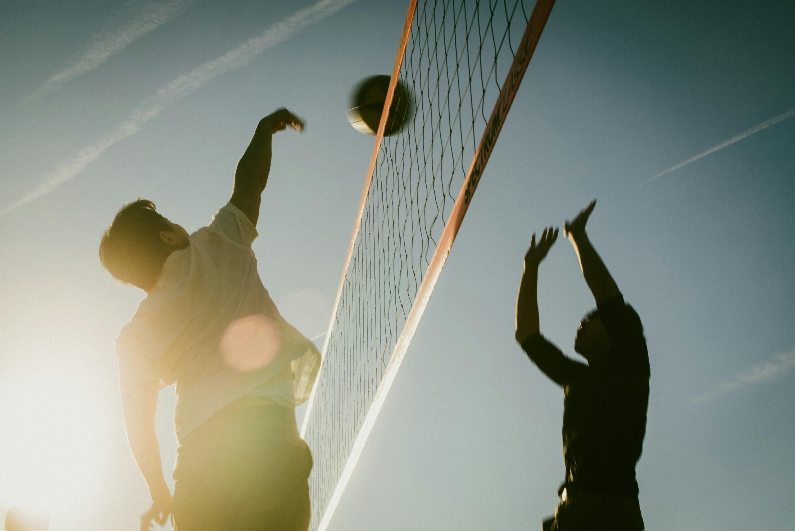 One volleyball player at either side of the net attempting to hit the ball above the net