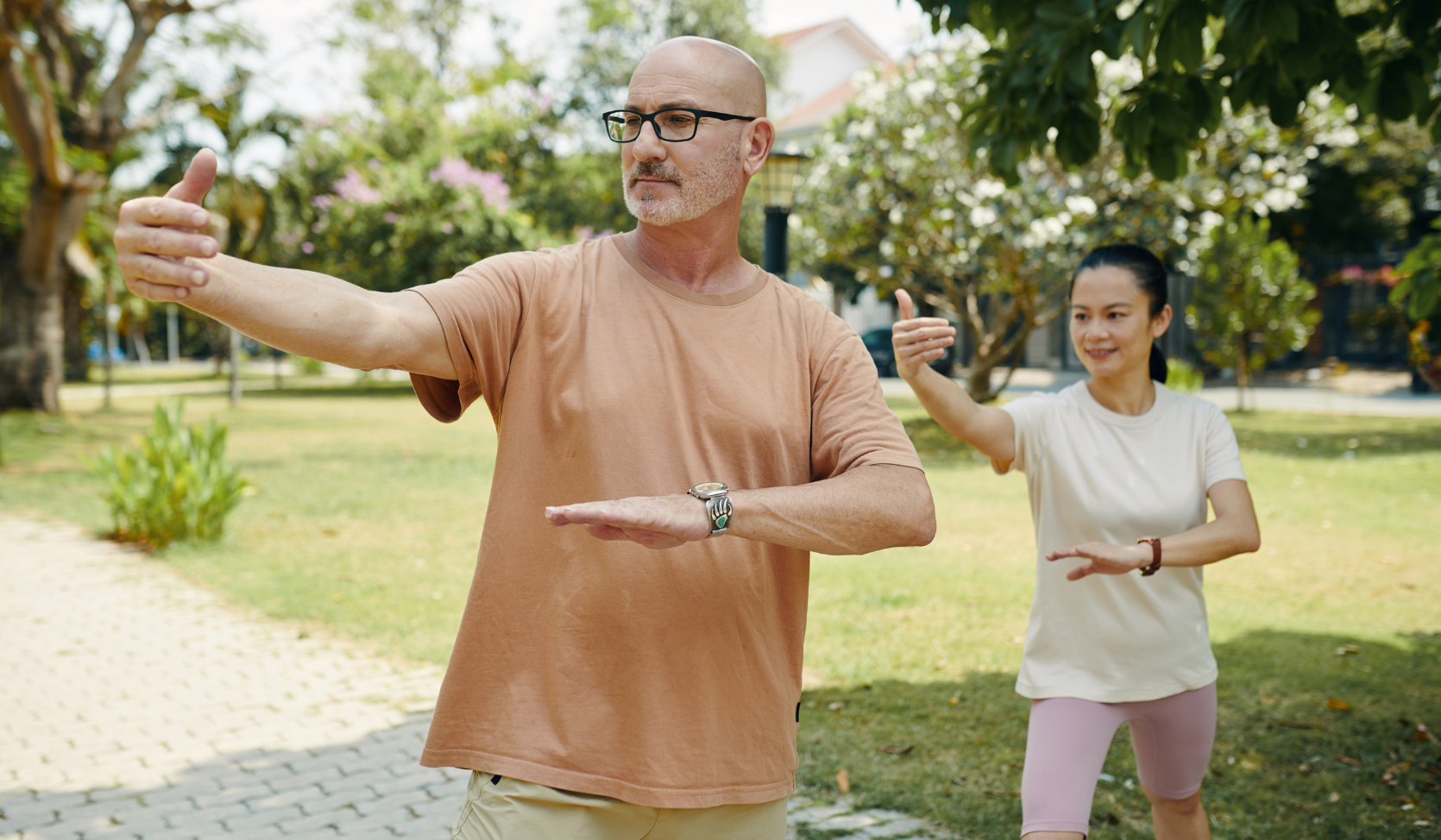 two people standing in a garden with trees doing tai chi